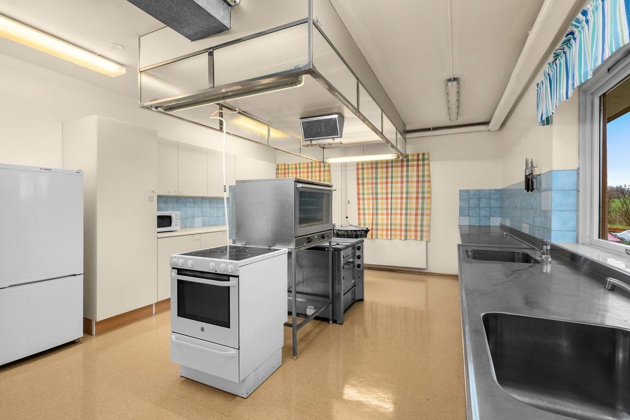 Industrikjøkken i underetasjen med hvite slette fronter og laminert benkeplate i kombinasjon med benkebeslag i rustfritt stål m/to kummer. Galleribilde