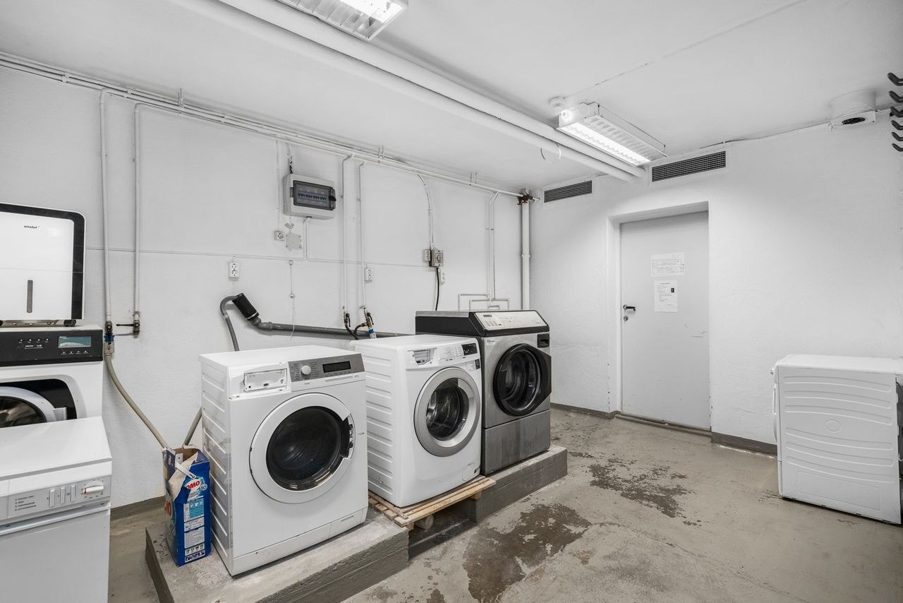 Vaskerom i underetasje med malt betonggulv og pusset og malte overflater. Sluk i støpejern. To skyllekummer i rustfritt stål og opplegg for tre vaskemaskiner. Galleribilde