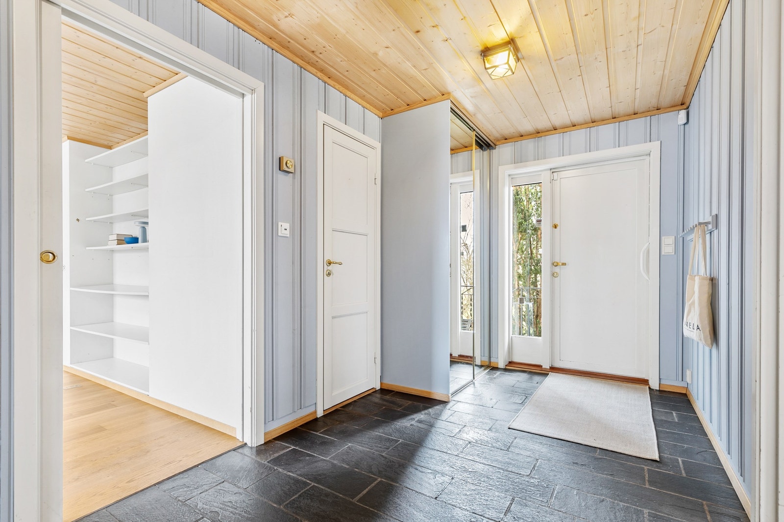 Romslig hall med fliser på gulvet. Det er elektrisk gulvvarme. Til høyre innenfor døren er det skyvedørsgarderobe med speilfronter til oppbevaring. Galleribilde