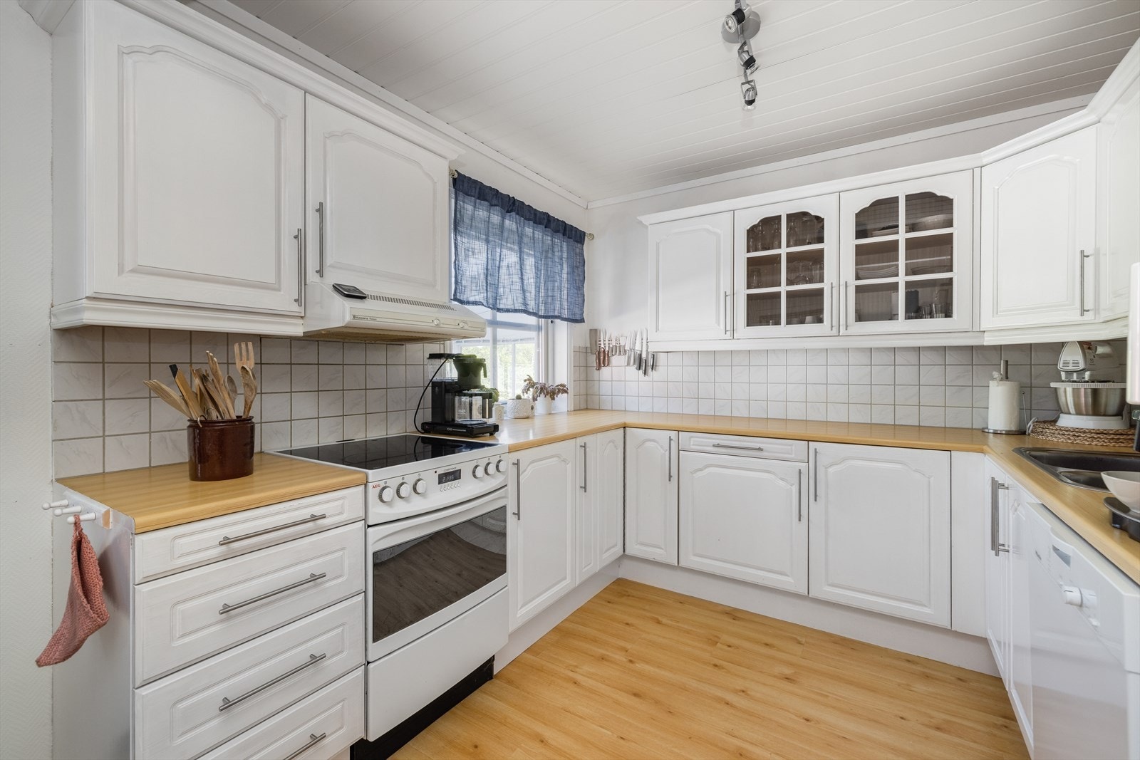 Innredningen har godt med skapplass og lyse fronter i profilert utførelse, samt vitrinefronter. Fliser over laminat benkeplate med gode arbeidsflater. Galleribilde