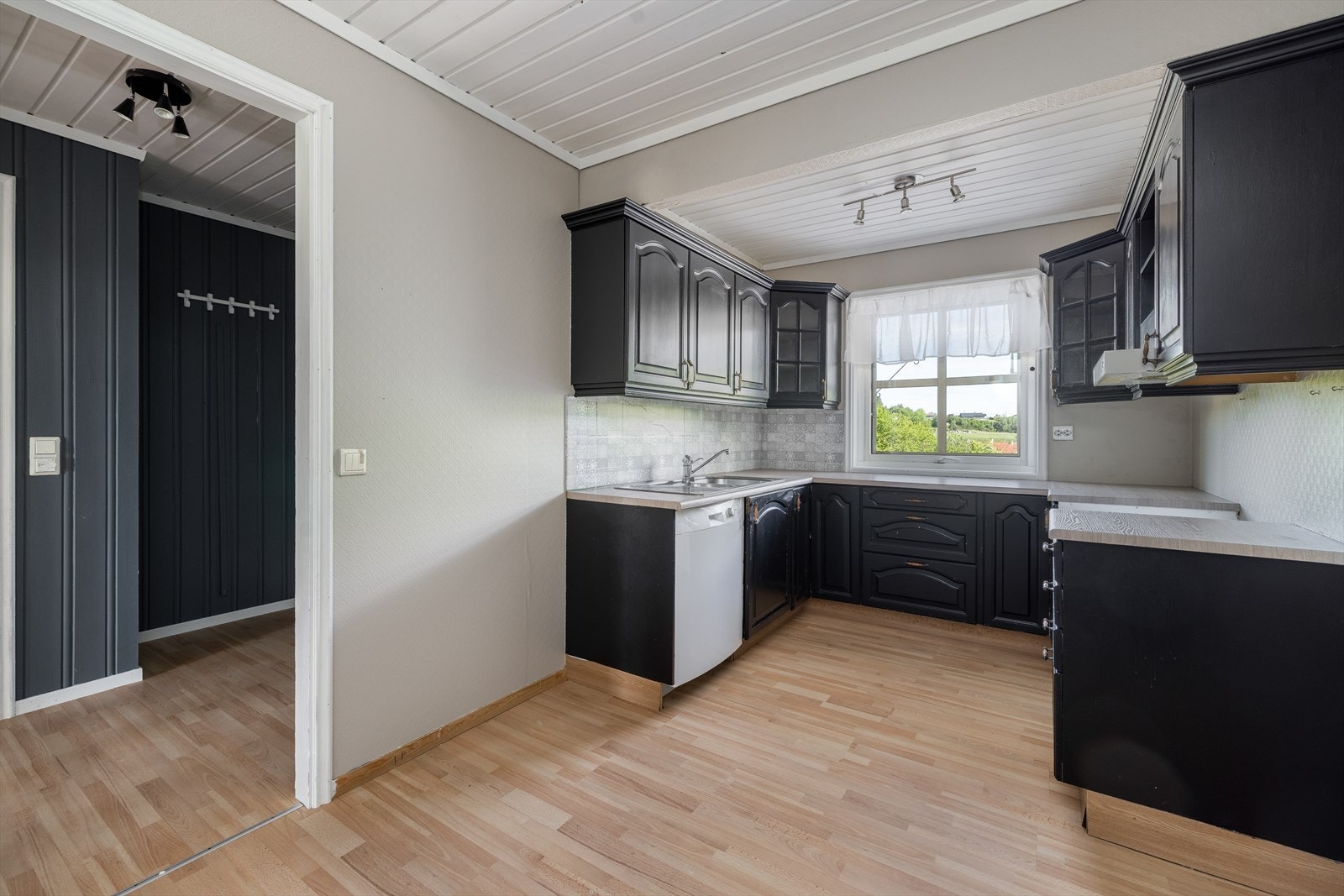 Stedvis flis over laminat benkeplate med gode arbeidsflater og nedfelt stålvask. Kjøkkenet er utstyrt med opplegg for oppvaskmaskin. Galleribilde