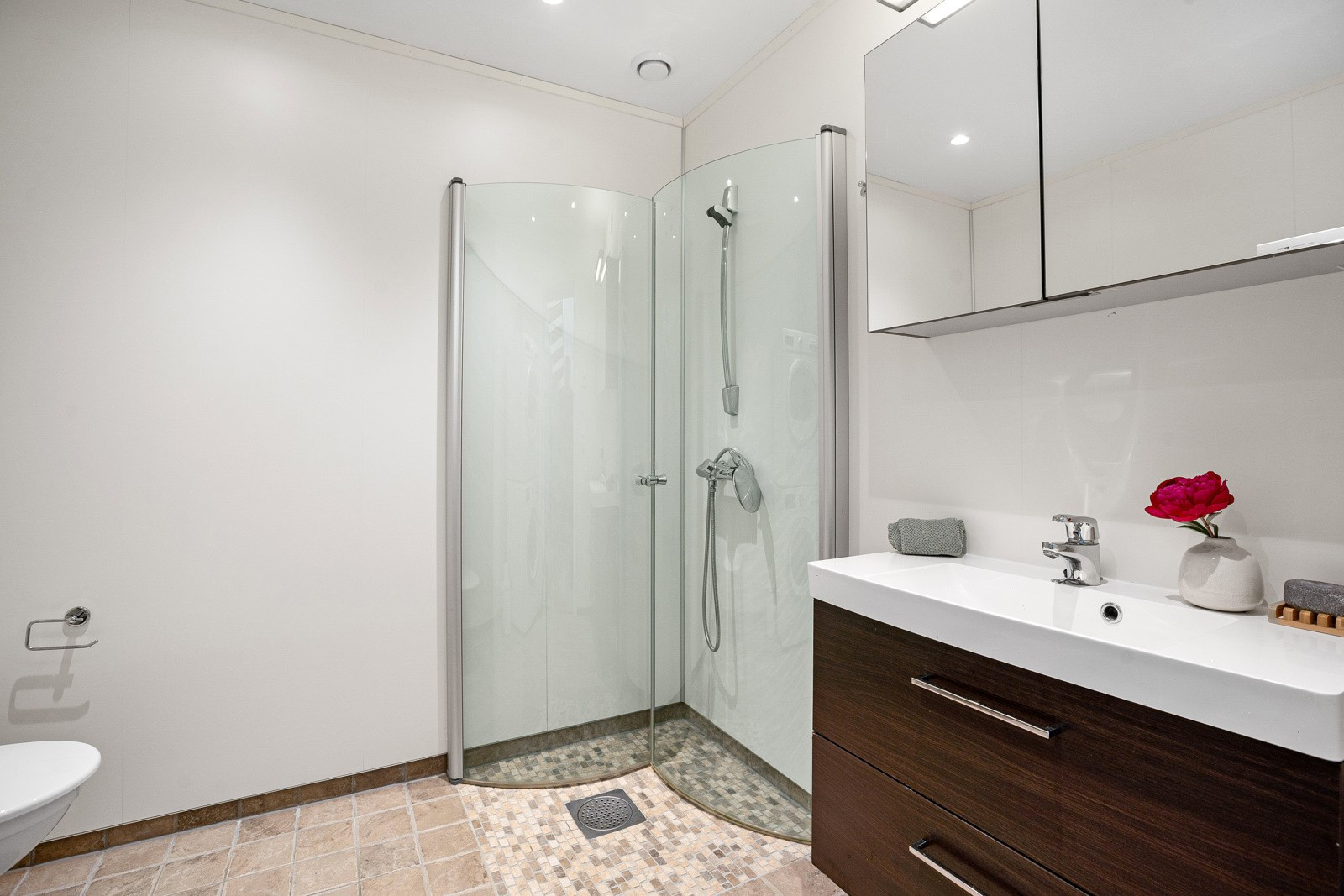 Praktisk bad/vaskerom med moderne baderomsinnredning, overspeil og dusjhjørne.