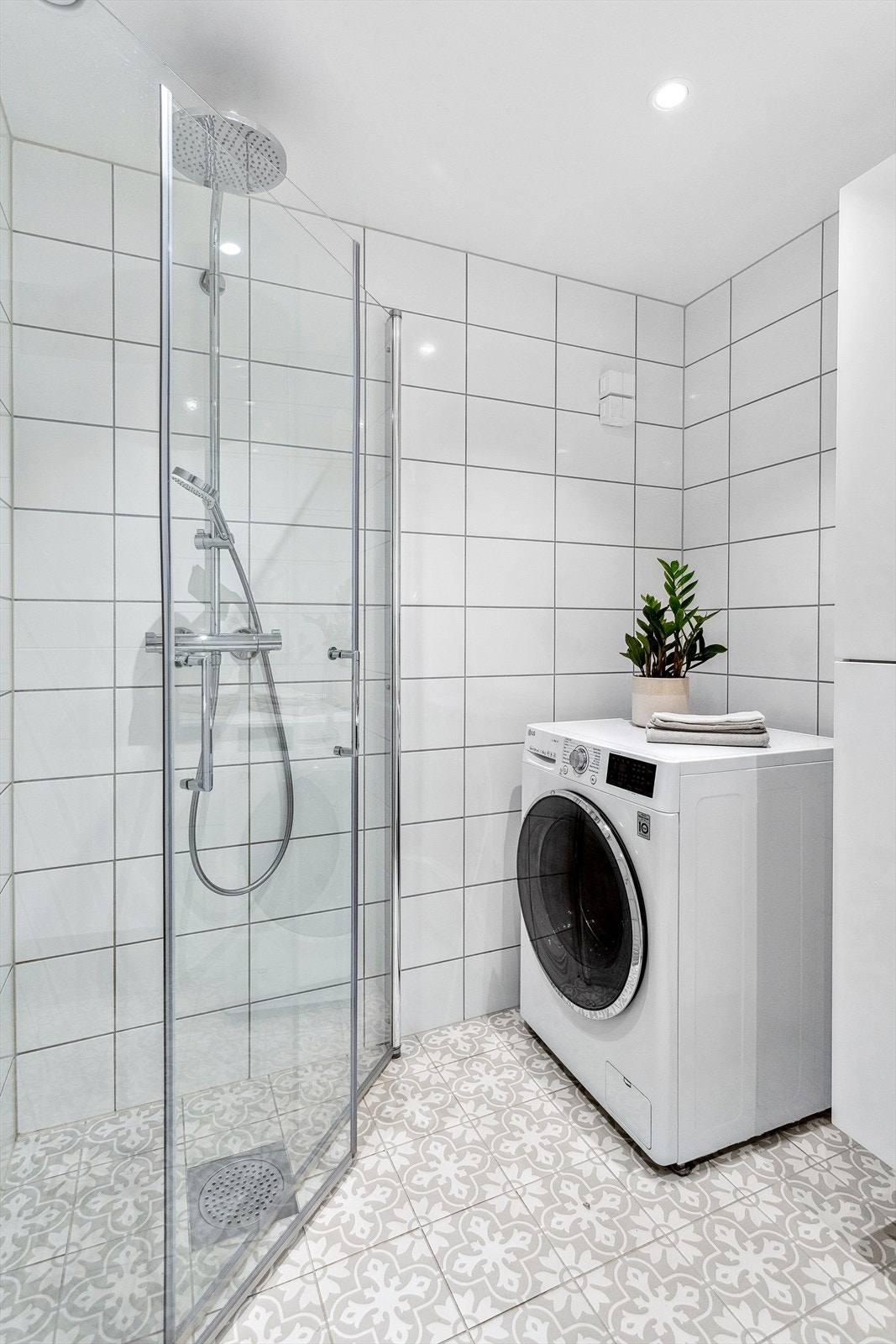 Badet har behagelig gulvvarme og store lyse fliser på vegg. Baderomsinnredningen består av benkeskap med glatte fronter og tilhørende høyskap i samme utførelse, dusj med innfellbare dører i herdet glass og opplegg for vaskemaskin. Galleribilde