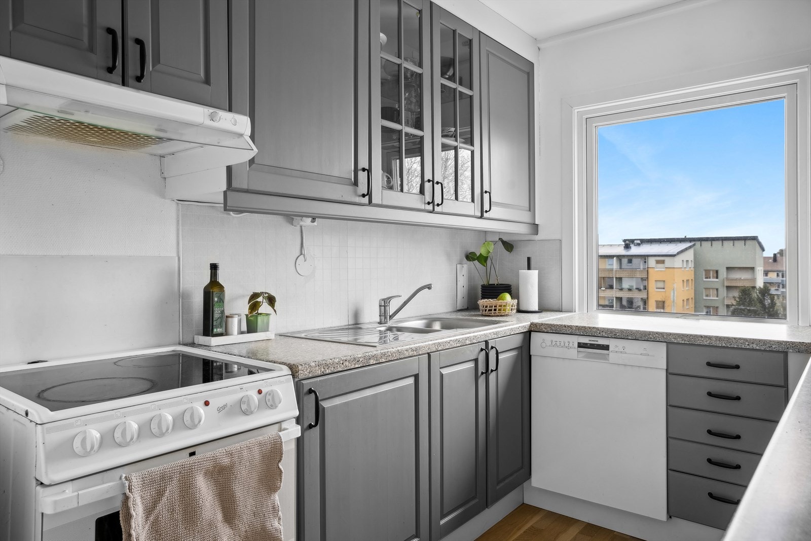 Kjøkken i grå utførelse med komfyr, oppvaskmaskin og kjøleskap som følger handel Galleribilde