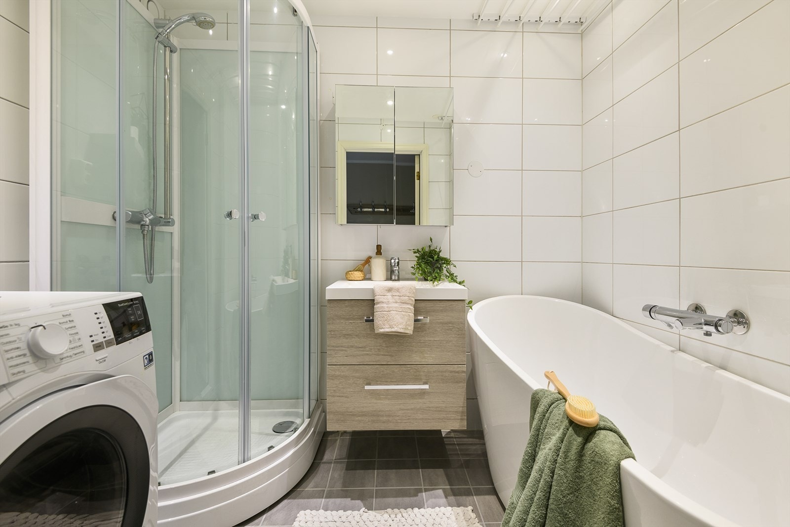 Pent og tiltalende bad med badekar, dusjkabinett og servantinnredning. Opplegg for vaskemaskin på badet. Galleribilde