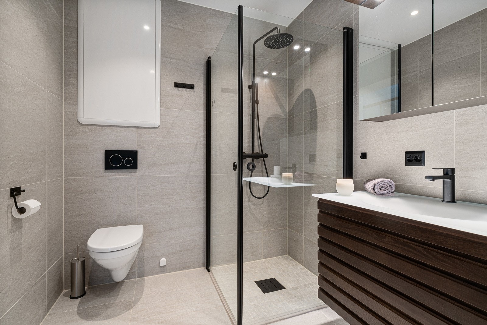 Badet er utstyrt med vegghengt toalett, servantinnredning og dusjhjørne i glass. Galleribilde