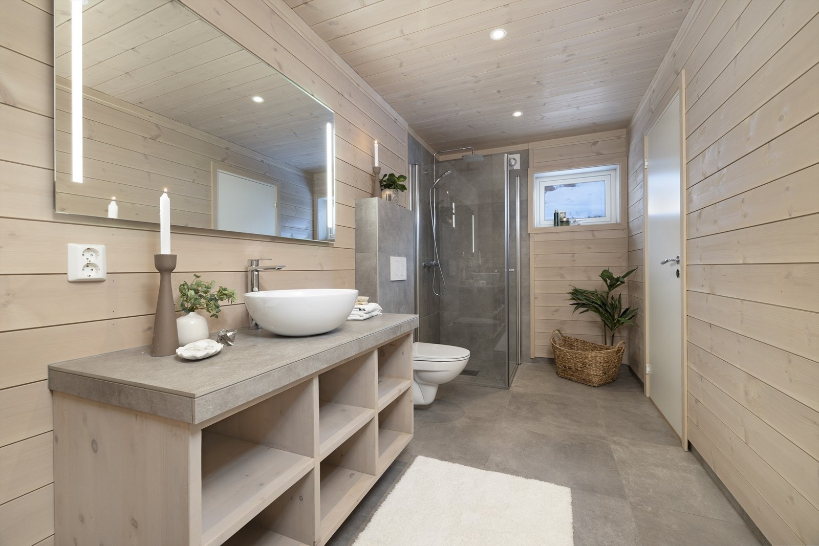 Lekkert bad innredet med innredning med bollevask, speil med integrert belysning, dusjhjørne og veggehengt toalett. Galleribilde