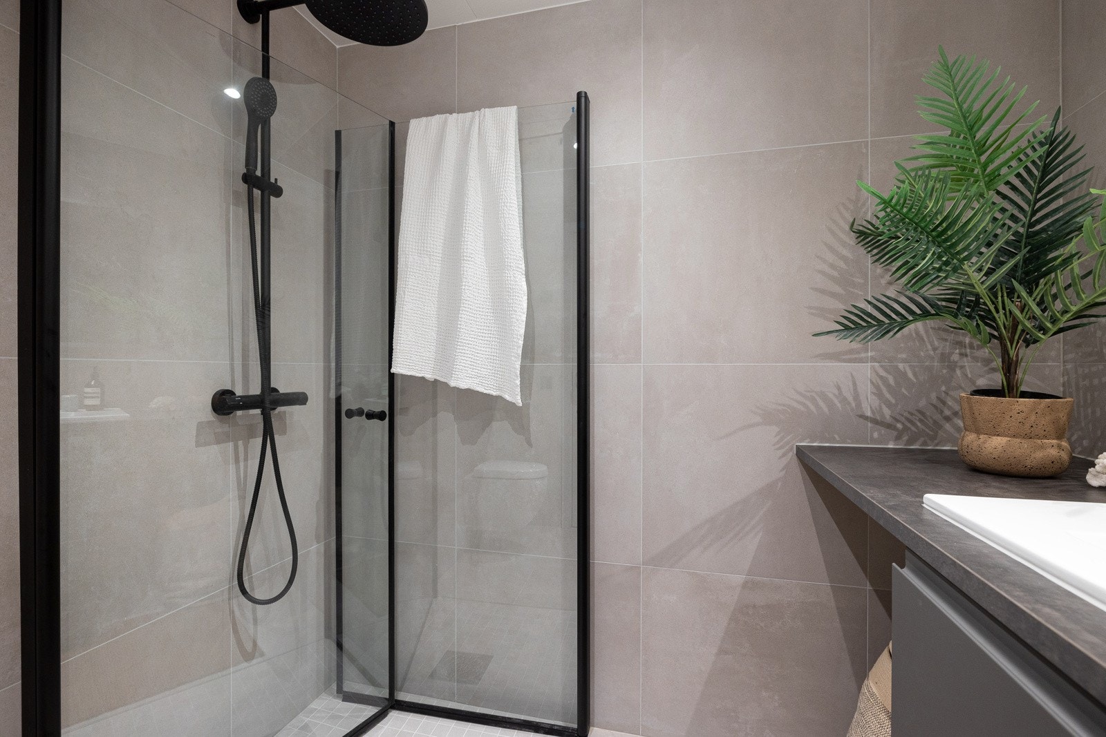 Badet har et vegghengt toalett med innebygget sisterne, servantskap med grå, glatte fronter, heldekkende laminert benkeplate (vegg-til-vegg), nedfelt porselenservant, ettgreps servantarmatur, speil og downlightsbelysning. Galleribilde