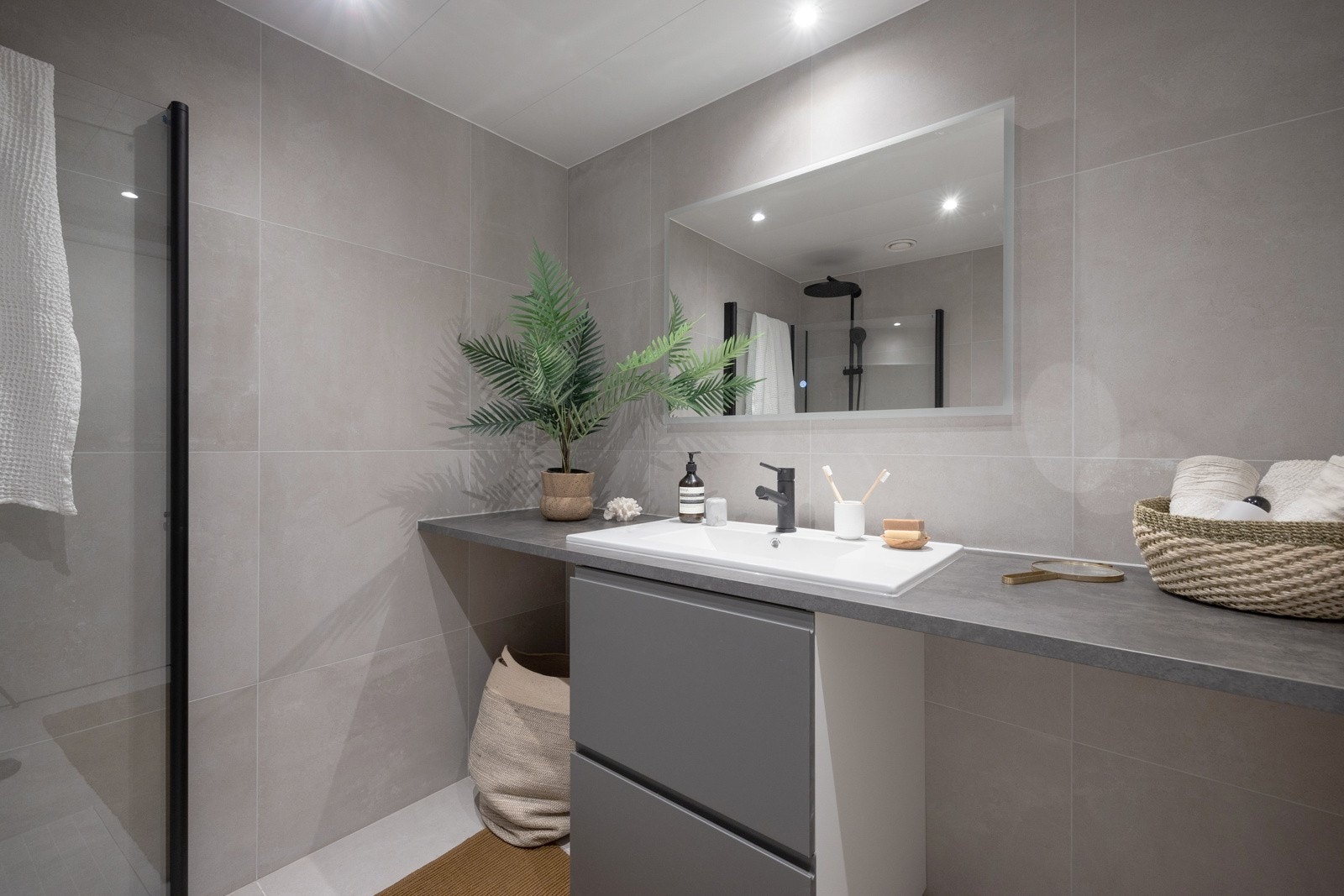 Videre er det dusjhjørne med nedfliset dusjsone og innfellbare glassdører, samt sort dusjbatteri, regndusj og hånddusj. Det er opplegg og plass for vaskemaskin under benkeplaten. Galleribilde