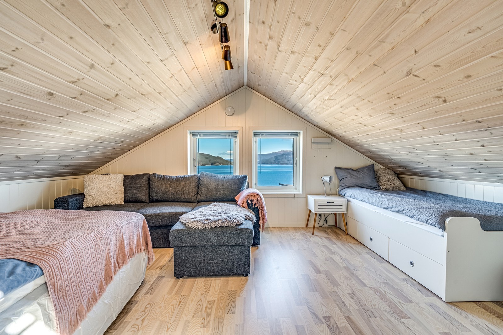 Soverom med persienner i vindu, enkeltseng med underskuffer, en dobbeltseng, sofa (kan omgjøres til dobbeltseng) og skrivepult plassert på dette rommet. Galleribilde