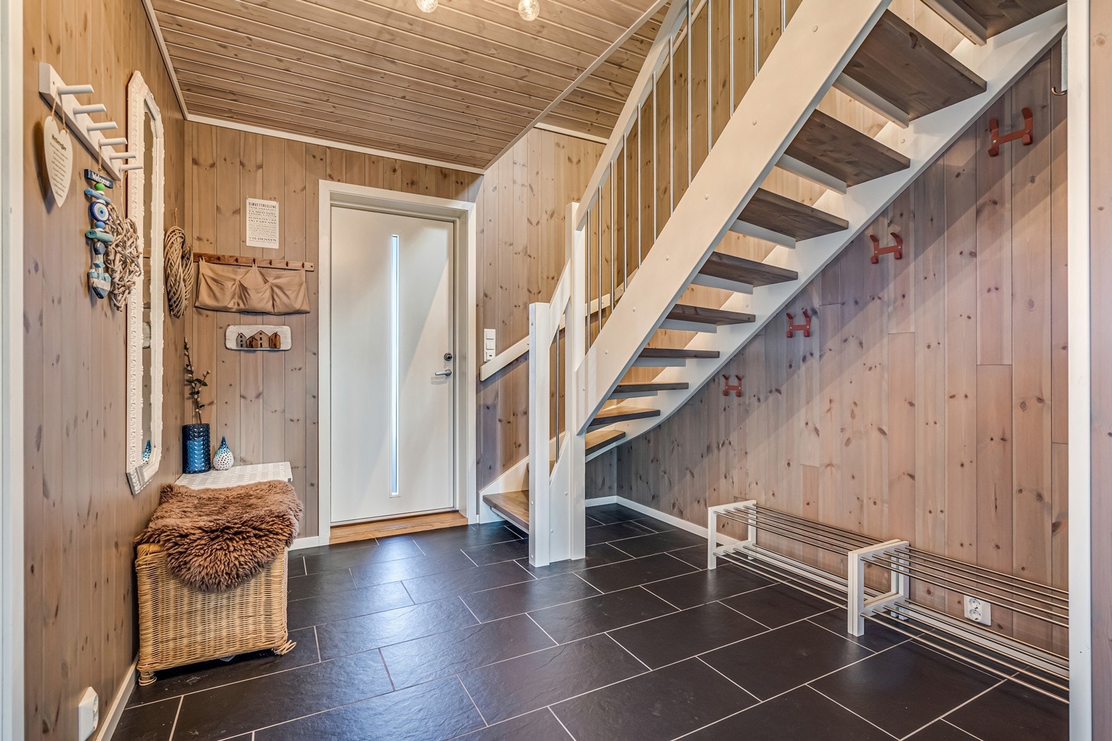 Gang med fliser og varmekabler på gulv, fint speil på veggen, trapp opp og varmepumpe som sprer varmen mellom etasjene. Galleribilde