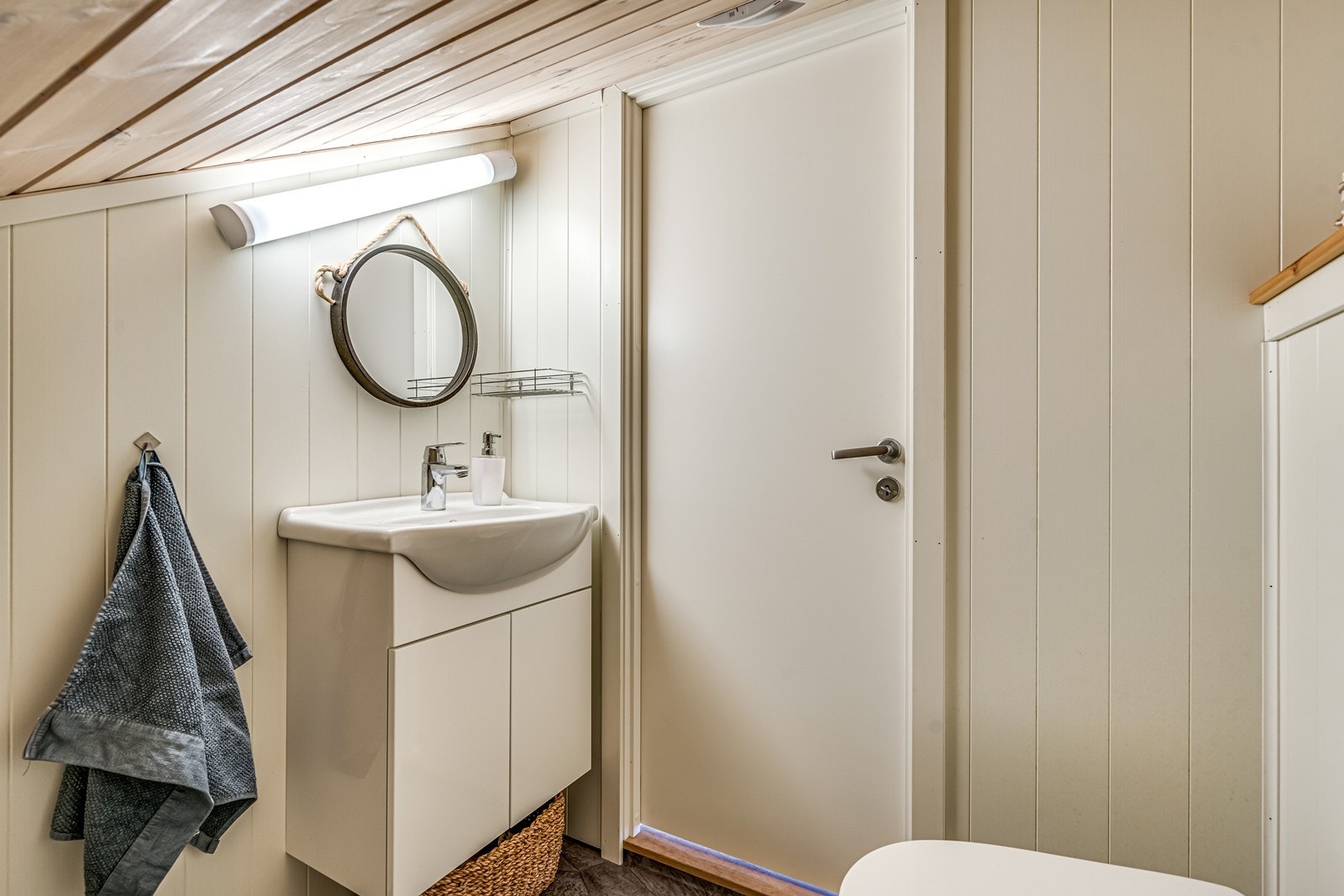 WC med belegg på gulv, vegghengt toalett, sluk, servant med underskap, speil, lys og elektrisk vifte. Galleribilde