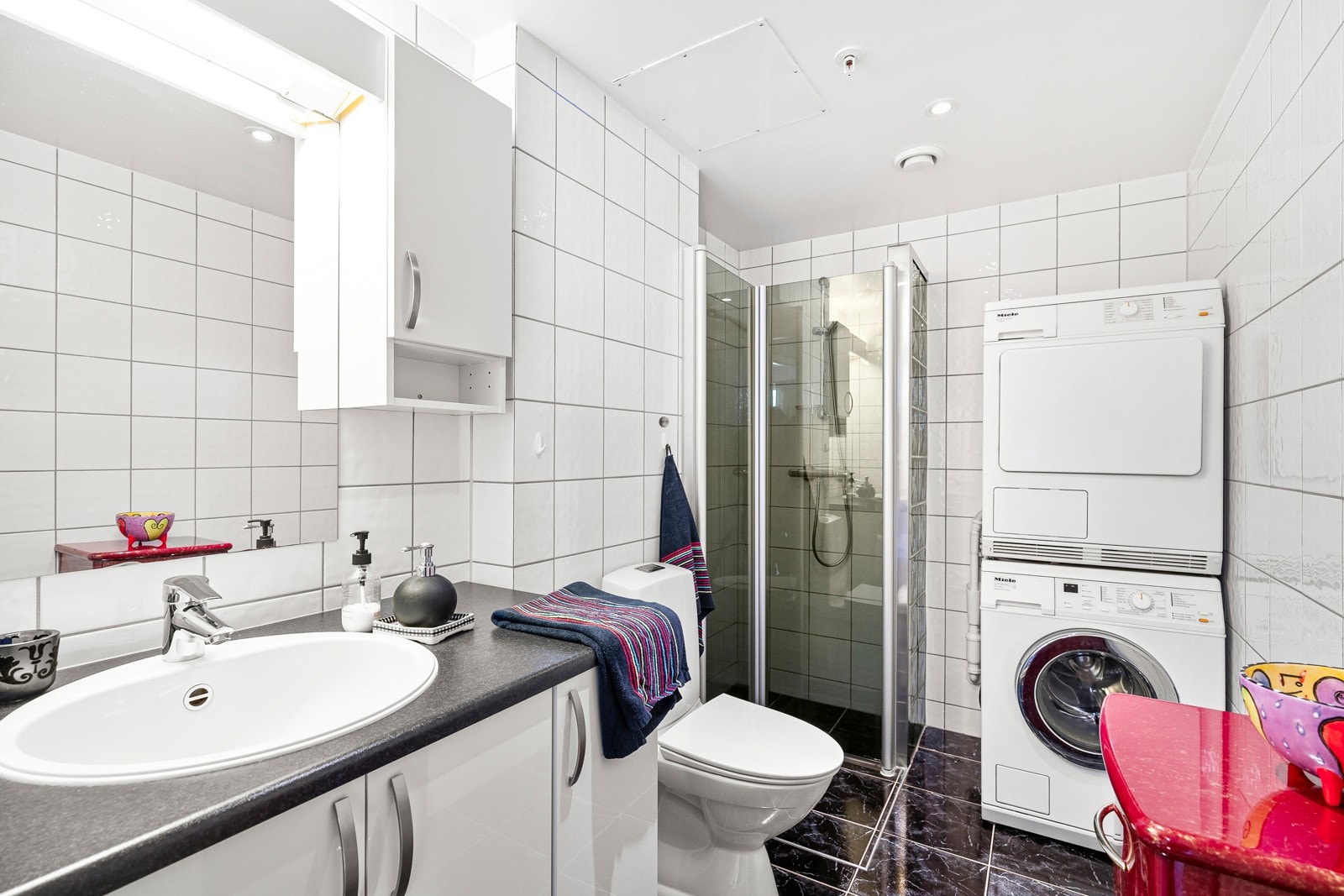 Badet er pent og helfliset. Det er innredet med seksjon med nedfelt servant, toalett og dusjhjørne. Galleribilde