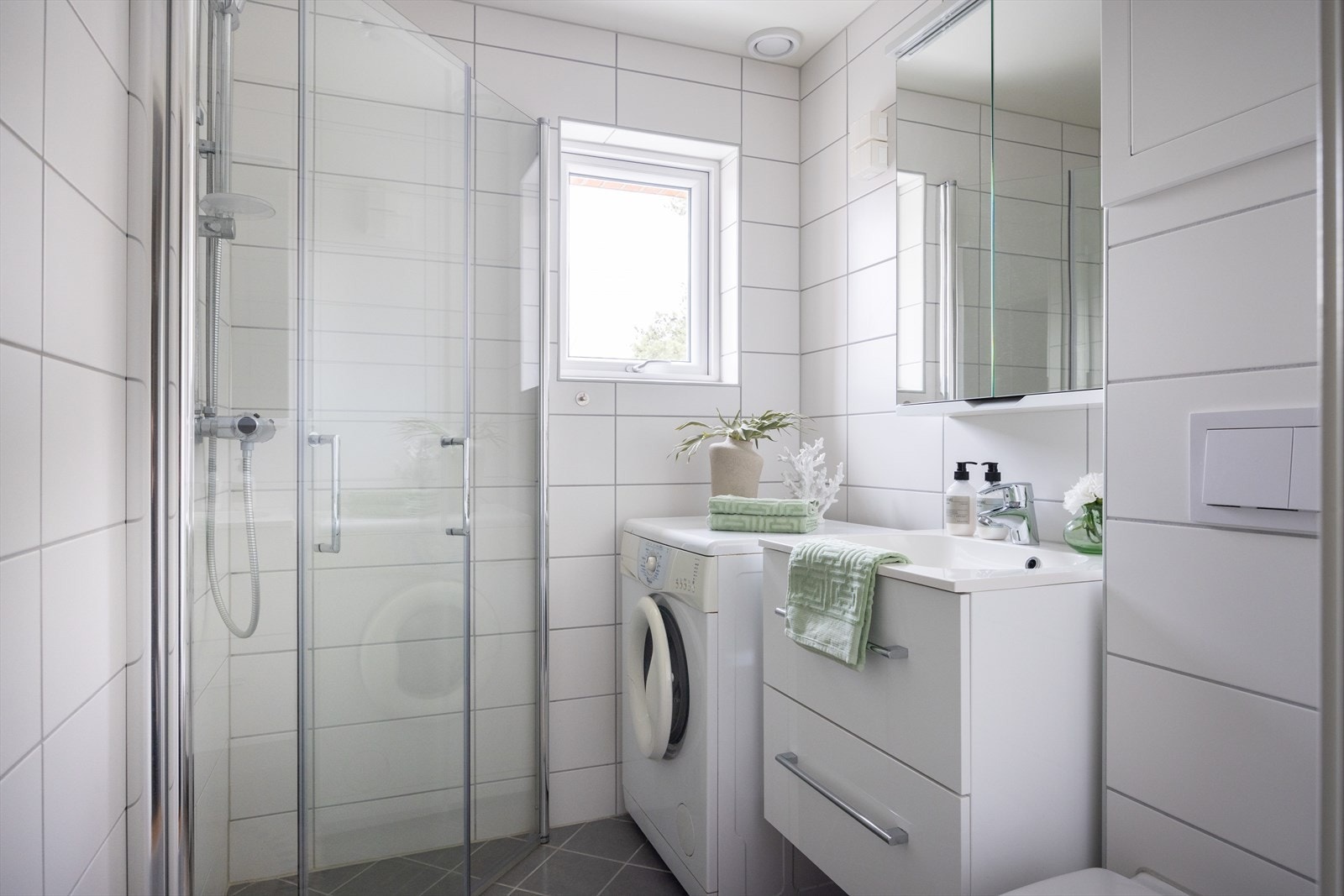Badet er innredet med vegghengt klosett, servant nedfelt i innredning, speilskap og dusjhjørne med svingbare glasdører. Det er opplegg for vaskemaskin. Galleribilde