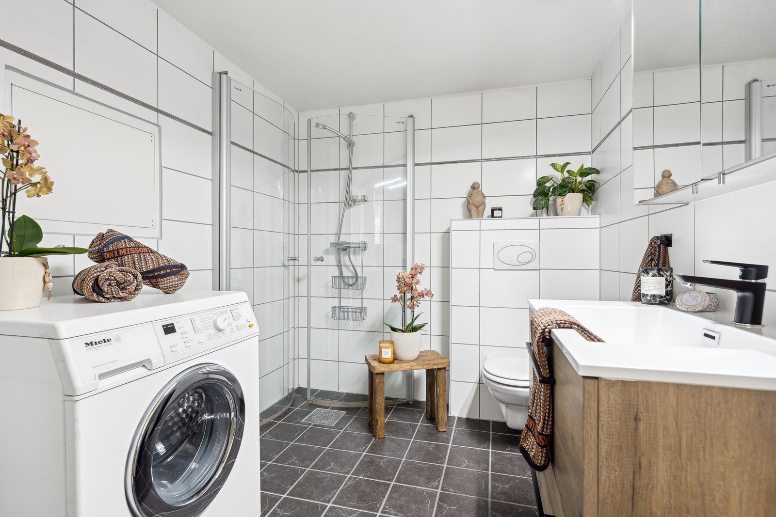 Lyst baderom fra 2006 med fliser på gulv og vegg. Innredning består av servant med underskap, ny fra 2023. Badet har også opplegg for vaskemaskin. Galleribilde