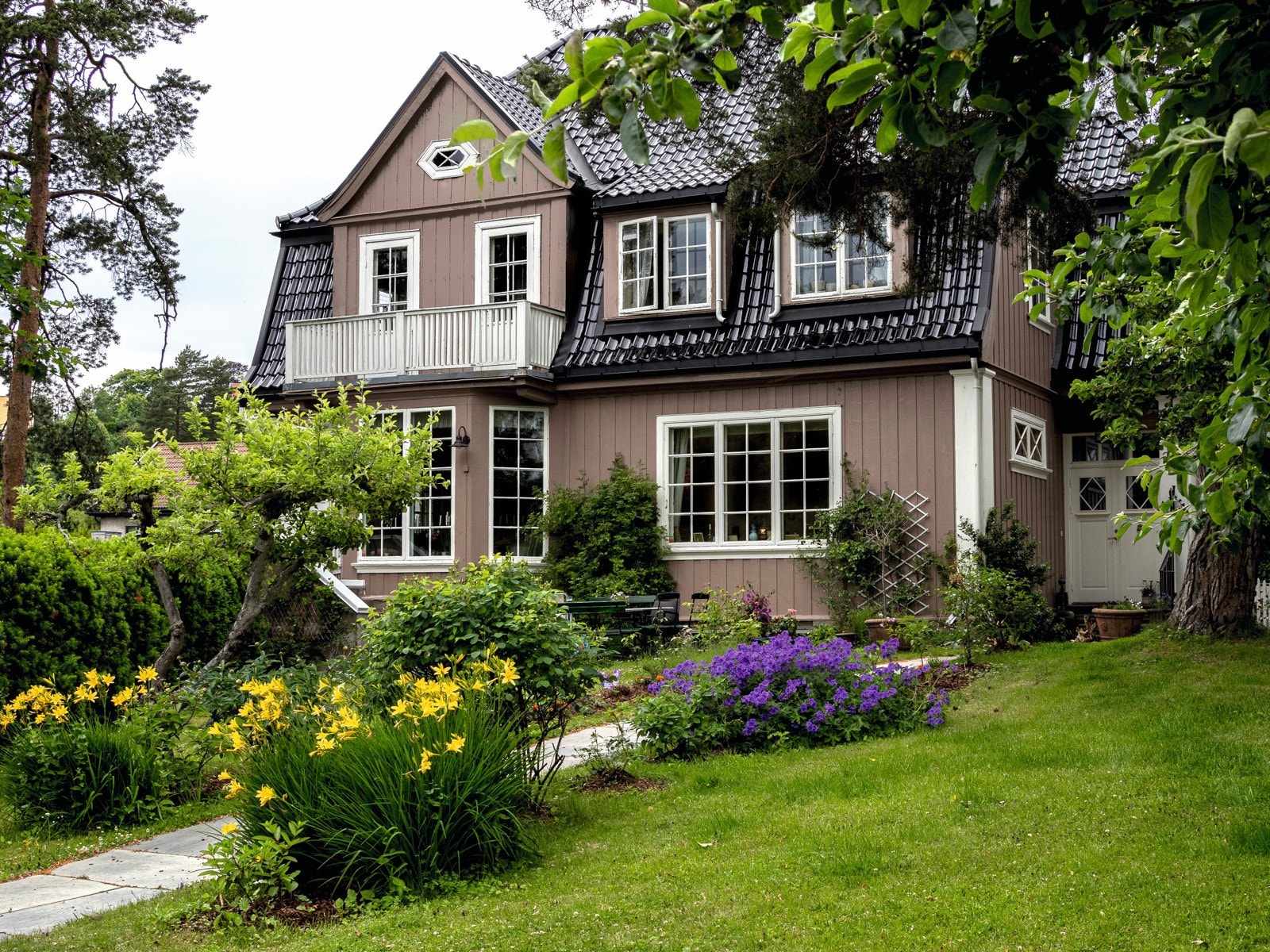 Et bilde av huset med frodig hage i full blomst. Galleribilde