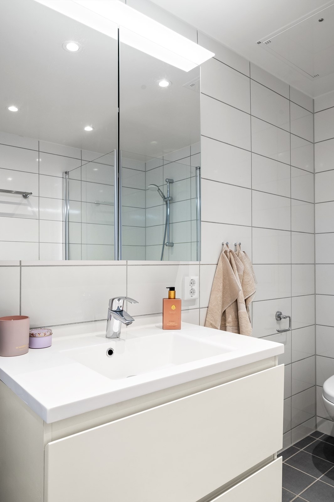 Badet er innredet med vegghengt toalett, servant nedfelt i innredning, speil med belysning, samt dusjhjørne med svingbare glassdører. Opplegg for vaskemaskin. Galleribilde