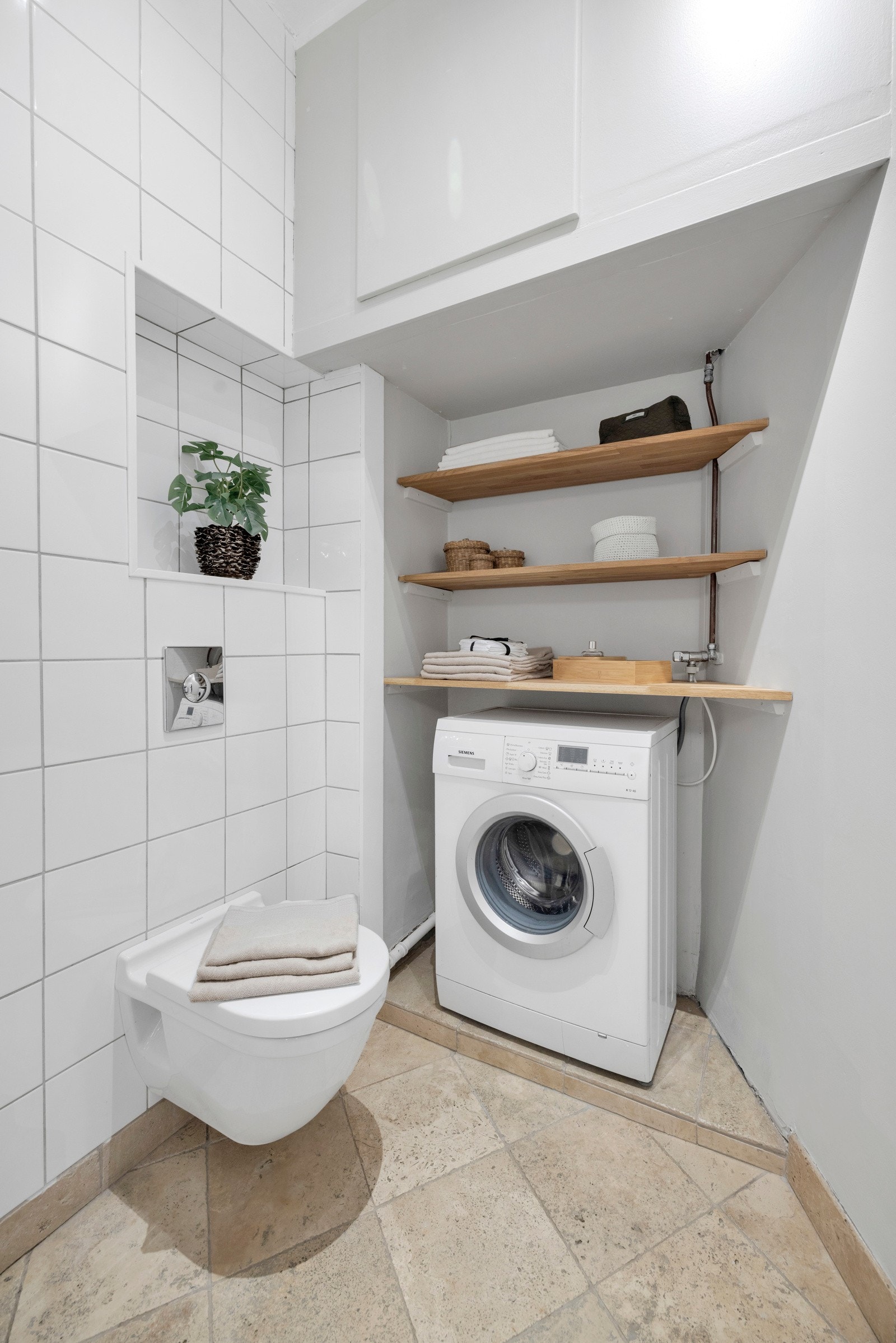 Badet har veggmontert toalett og nisje med opplegg for vaskemaskin. Galleribilde