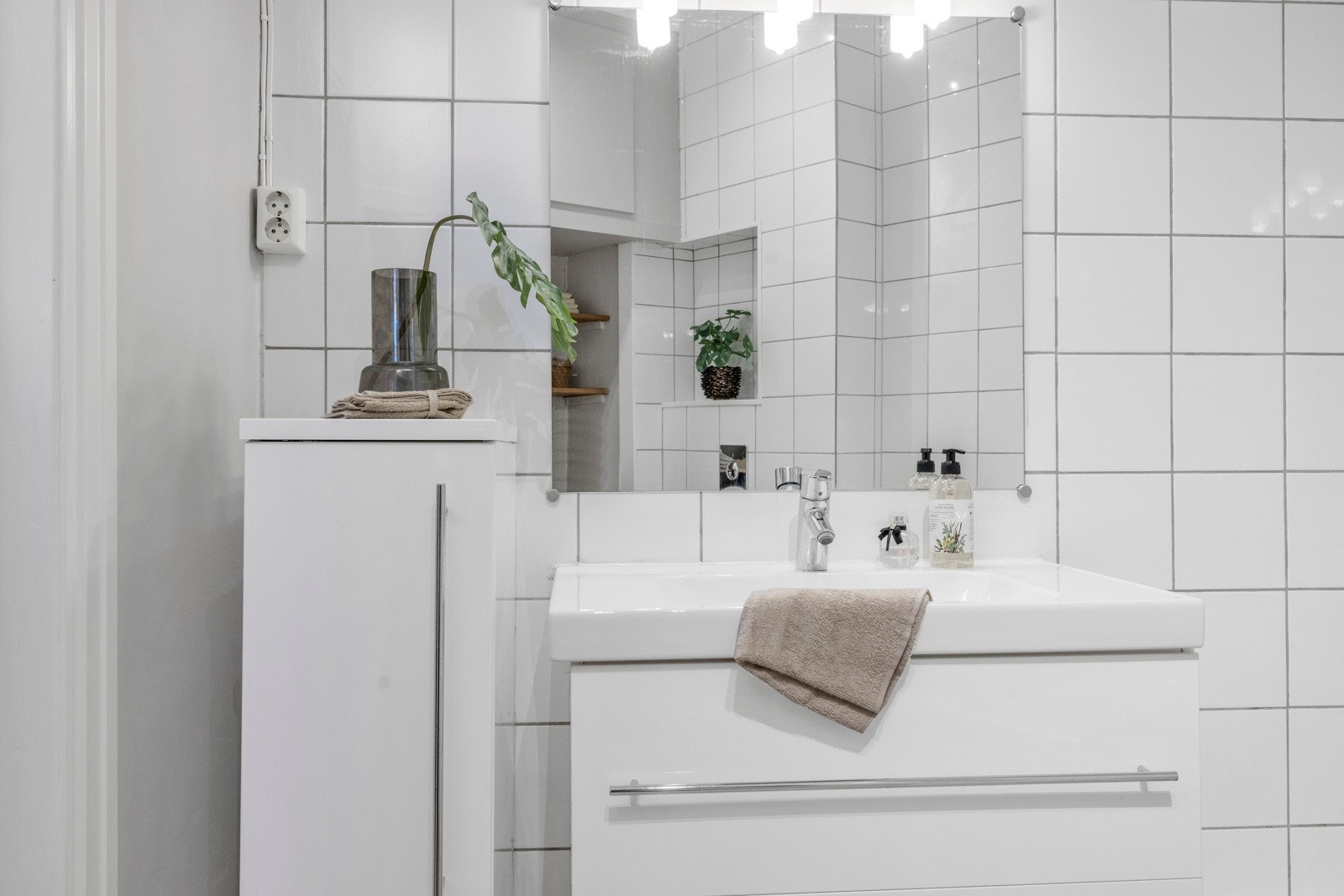 Badet har hvitt skap og skuffeseksjon, speil med overlys, badekar og veggmontert toalett. Galleribilde