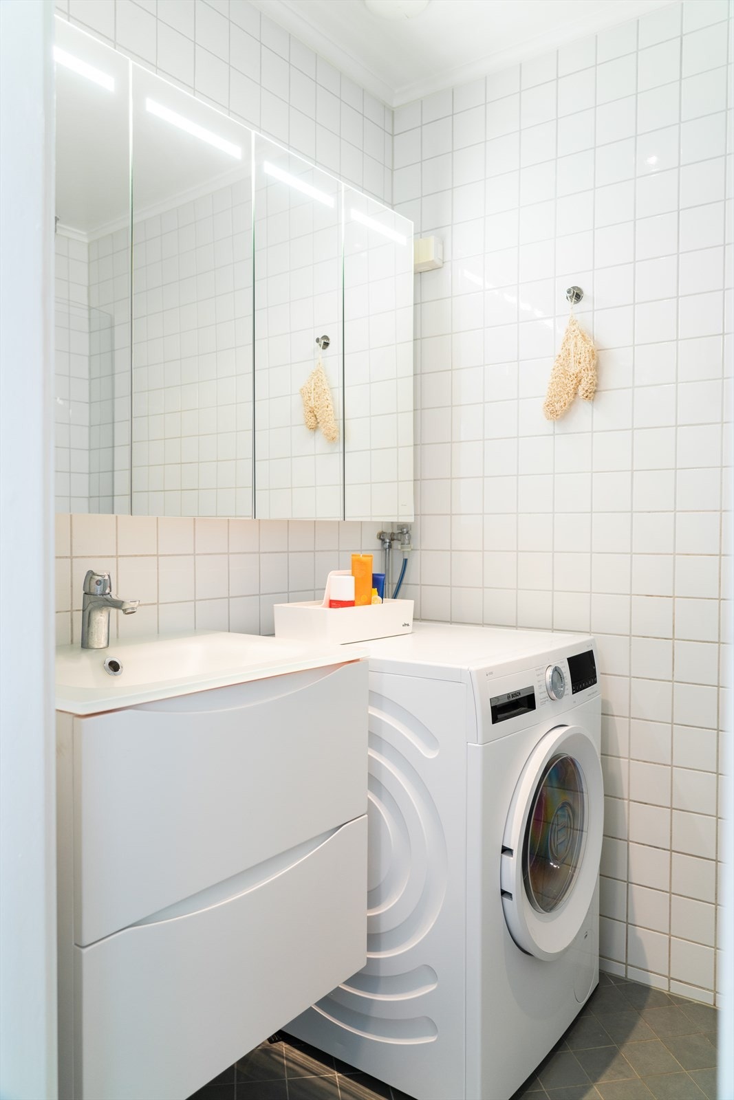 Badet er utstyrt med et veggmontert toalett, et dusjhjørne med en buet glassdør samt opplegg for vaskemaskin. Servantinnredning og et romslig speilskap fra Vikingbad ble satt inn i 2022. Galleribilde