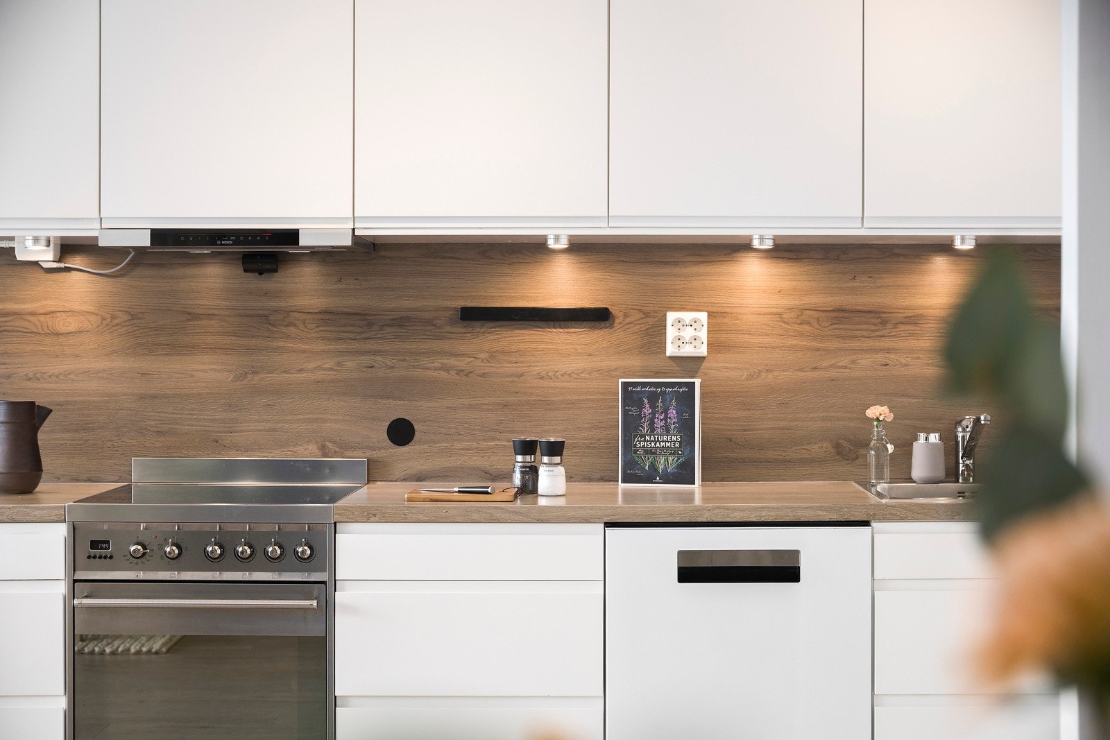 Hvite glatte fronter og en lekker benkeplate med matchende backsplash gir kjøkkenet et delikat preg Galleribilde