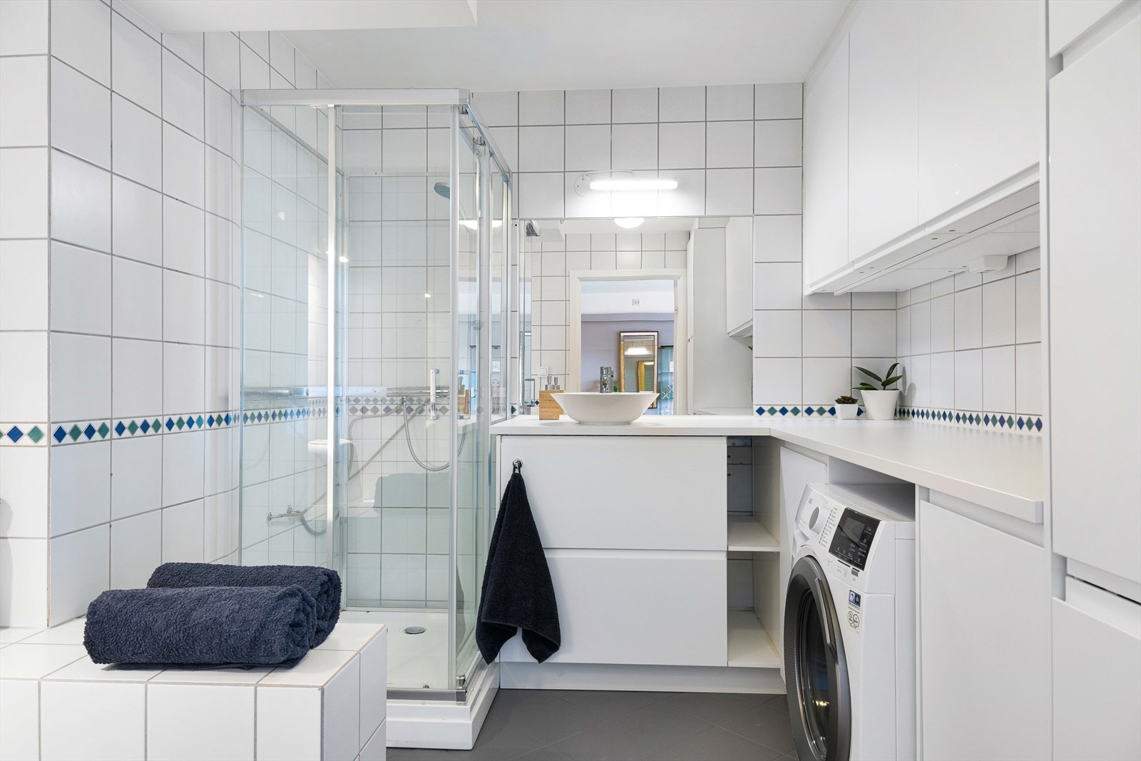 Badet er innredet med servant på skuffeinnredning, overskap, speil med belysning, dusjkabinett samt gulvmontert toalett. Galleribilde