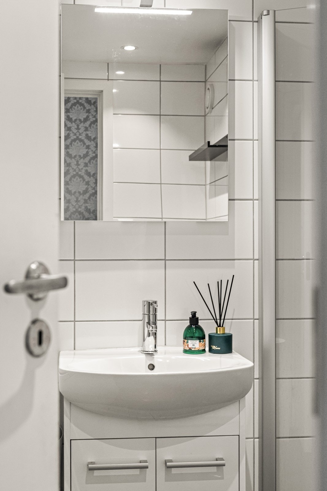 Badet utstyrt med vegghengt toalett, servant med overhengende speil og dusjsone med inn- og utfeltbare dusjvegger. Galleribilde