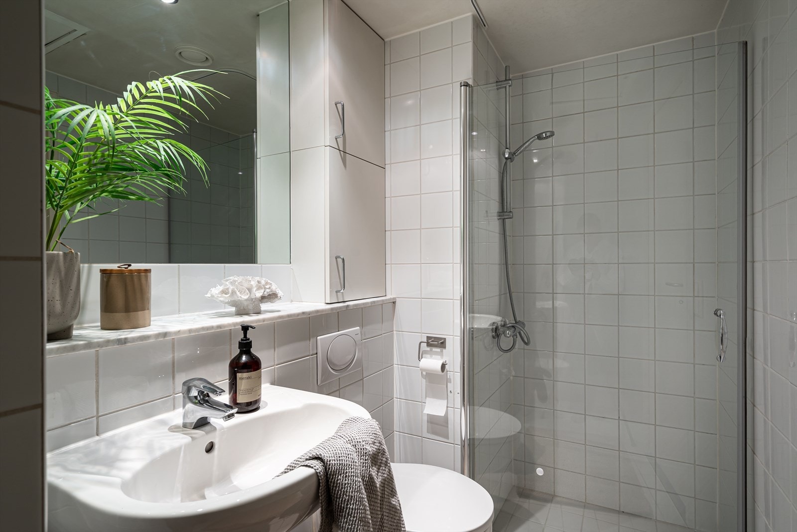 Pent og tidløst baderom fra byggeår. Innredet med speil, skap for oppbevaring, vegghengt toalett og dusjsone med glassdør. Galleribilde