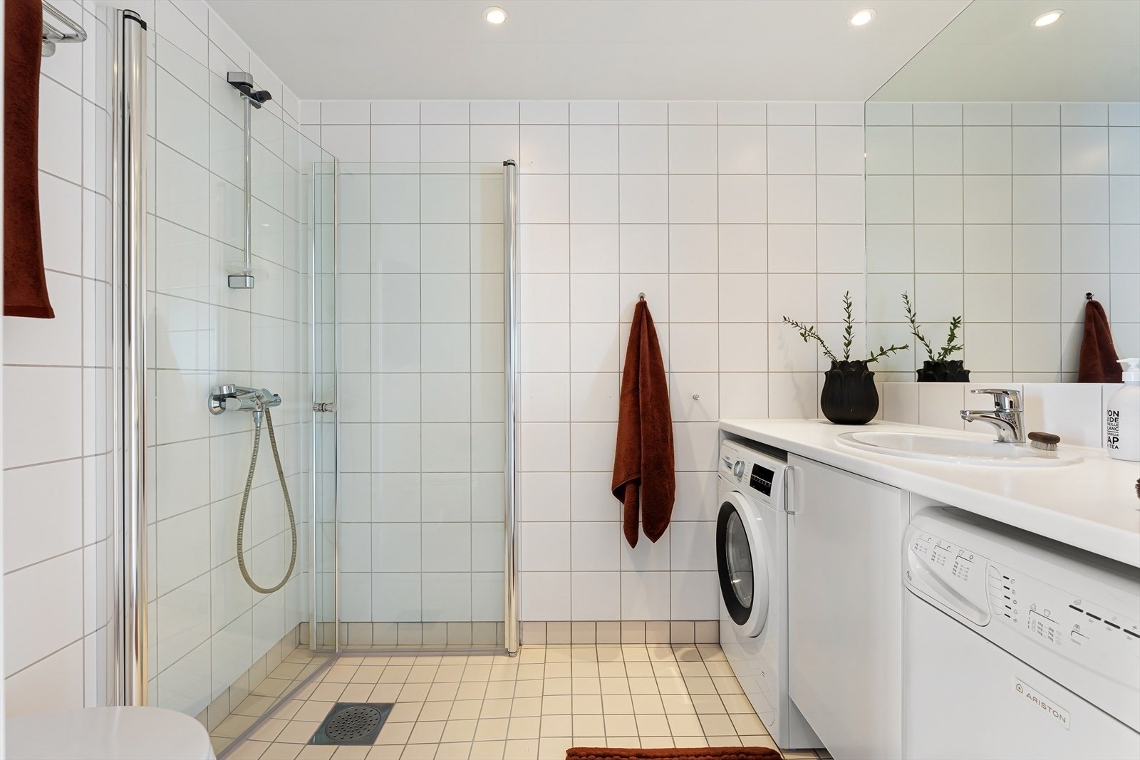 Badet har innredning med nedfelt servant, stort innfelt speil, veggmontert toalett og dusjvegger i hjørnet Galleribilde