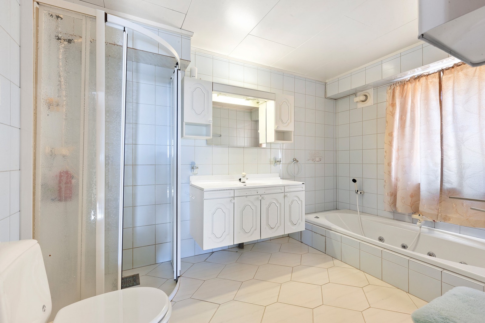 Badet har lys innredning med nedfelt servant og skap under, overskap og speil med lys over, dusjhjørne, badekar og toalett. Varme i gulv gir en lun start på dagen Galleribilde