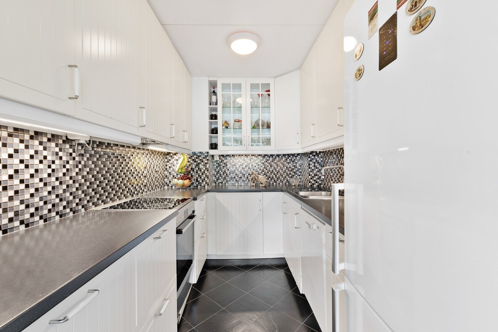 Pent kjøkken med profilerte fronter og laminat benkeplate i rustfritt stål. Galleribilde