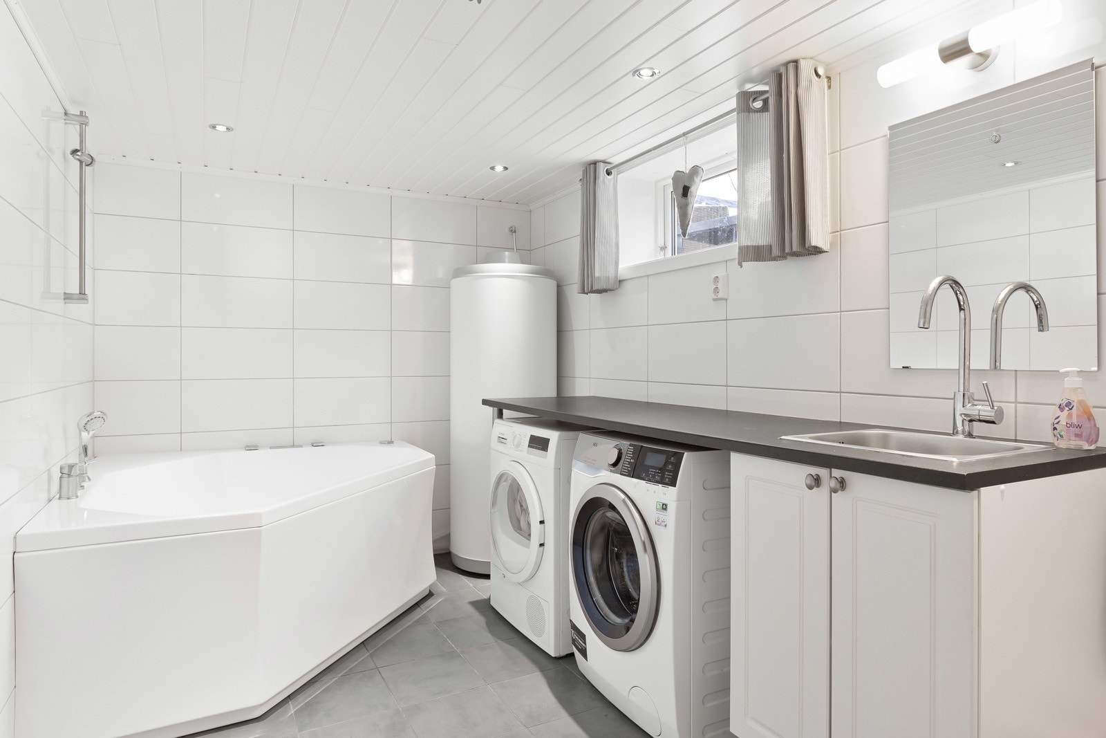 fliser på gulv, vegger og mdf panel i himling. Vaskerom er utstyrt med vaskeromsinnredning med plass til vaskemaskin og tørketrommel, hjørnebadekar, vegghengt toalett og varmtvannsbereder. Det er montert varmekabler i gulv og spotter i himling. Galleribilde