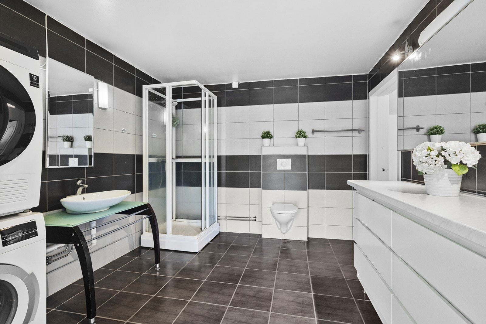 Badet er utstyrt med dusjkabinett, vegghengt wc og åpen servantinnredning. Det er lunende varmekabler i gulvet. Galleribilde
