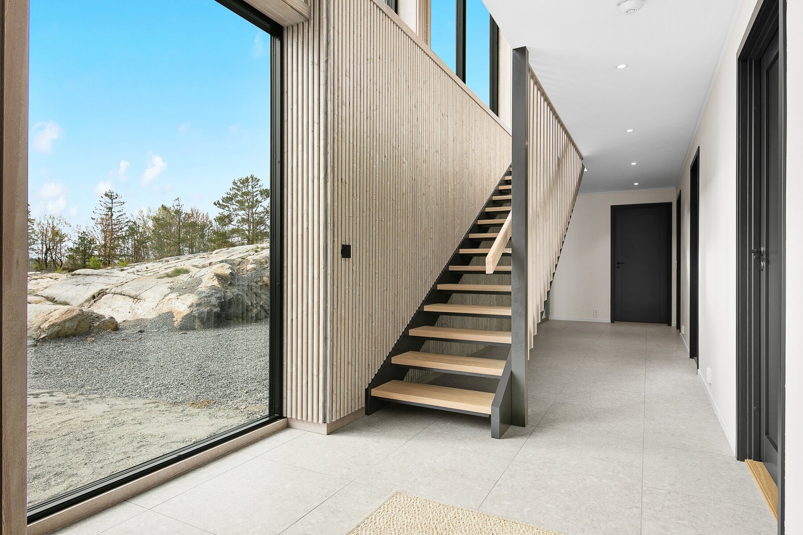 Trappegang med tøffe detaljer som spilevegg, flott trapp og et stor vindu mot gårdsplassen. Galleribilde