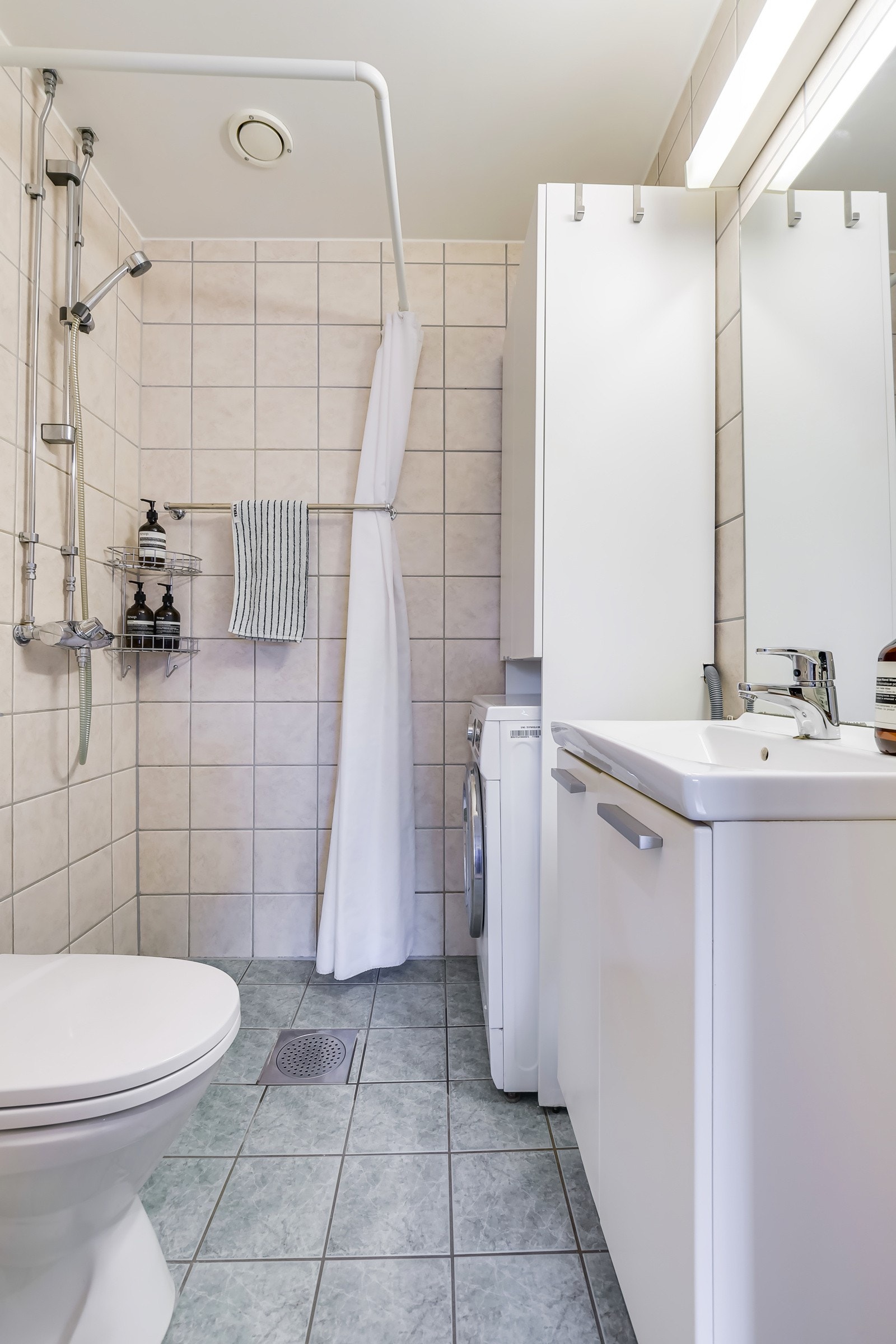 Flislagt bad med toalett, servant, dusj og opplegg for vaskemaskin. Galleribilde