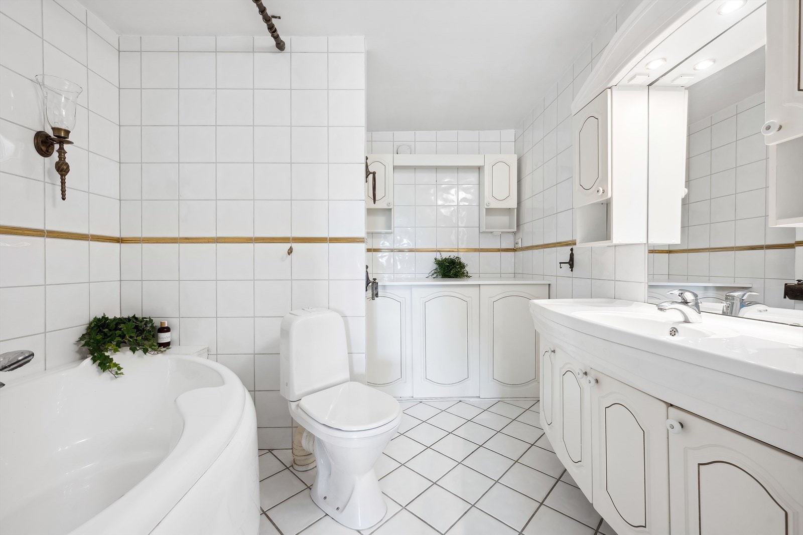 Romslig flislagt bad, utstyrt med badekar, gulvstående wc og servantinnredning med under- og overskap. I tillegg er det en ekstra oppbevaringsmodul samt opplegg og plass til vaskemaskin Galleribilde