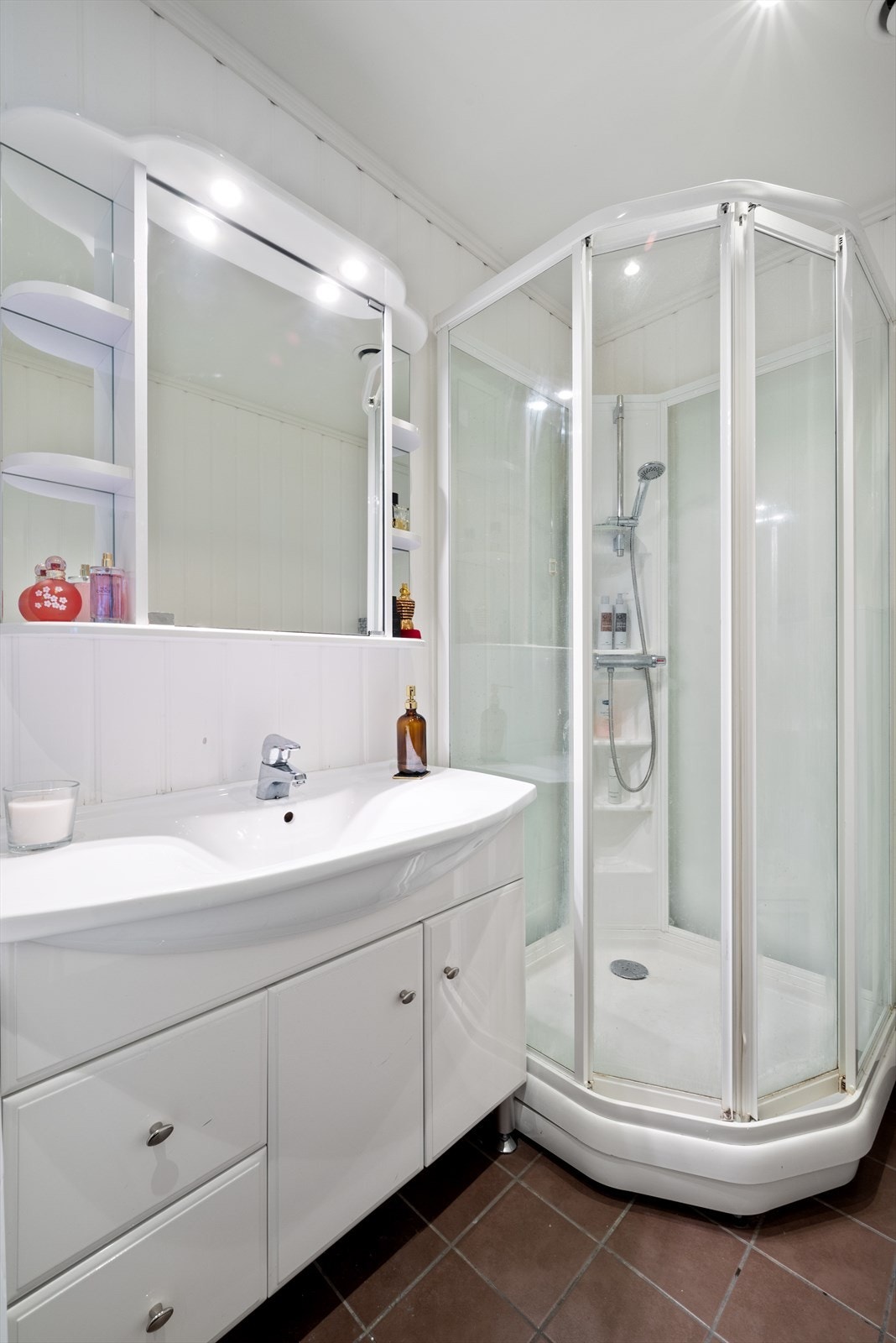 Her får du flislagt gulv med varmekabler, hvitmalte panelplater på vegger, vegghengt wc, dusjkabinett, uttak til vaskemaskin og servantinnredning med integrert speil over. Galleribilde