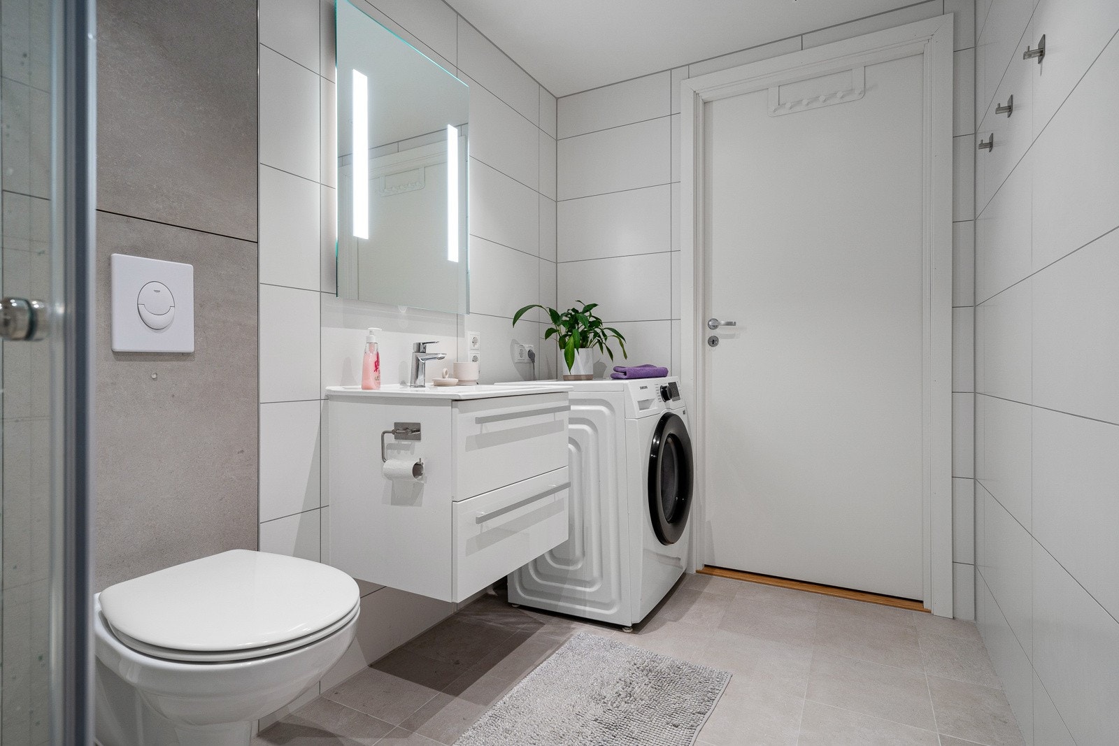 Badet er utstyrt med dushjørne med innfellbare dører, vegghengt toalett, vegghengt baderomsinnredning og opplegg til vaskemaskin. Galleribilde