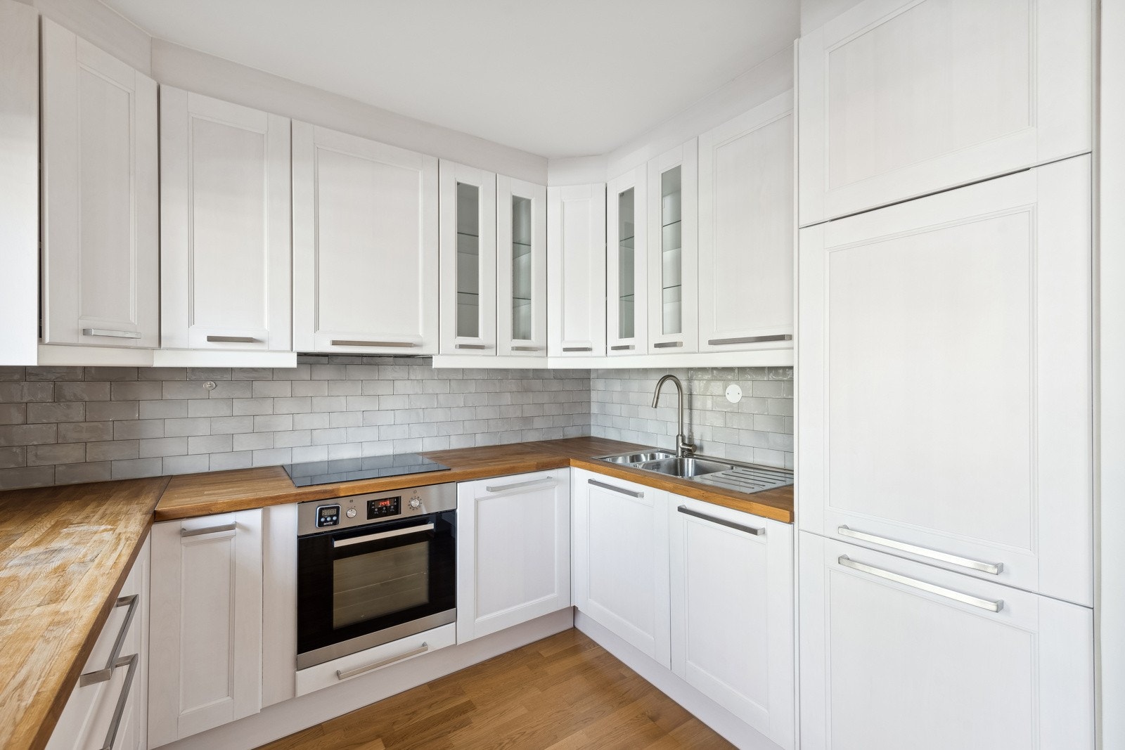 Takhøy innredning med profilerte fronter og to vitrinedører. Heltre benkeplate med fliser over. Alle hvitevarer er integrerte og medfølger. Galleribilde