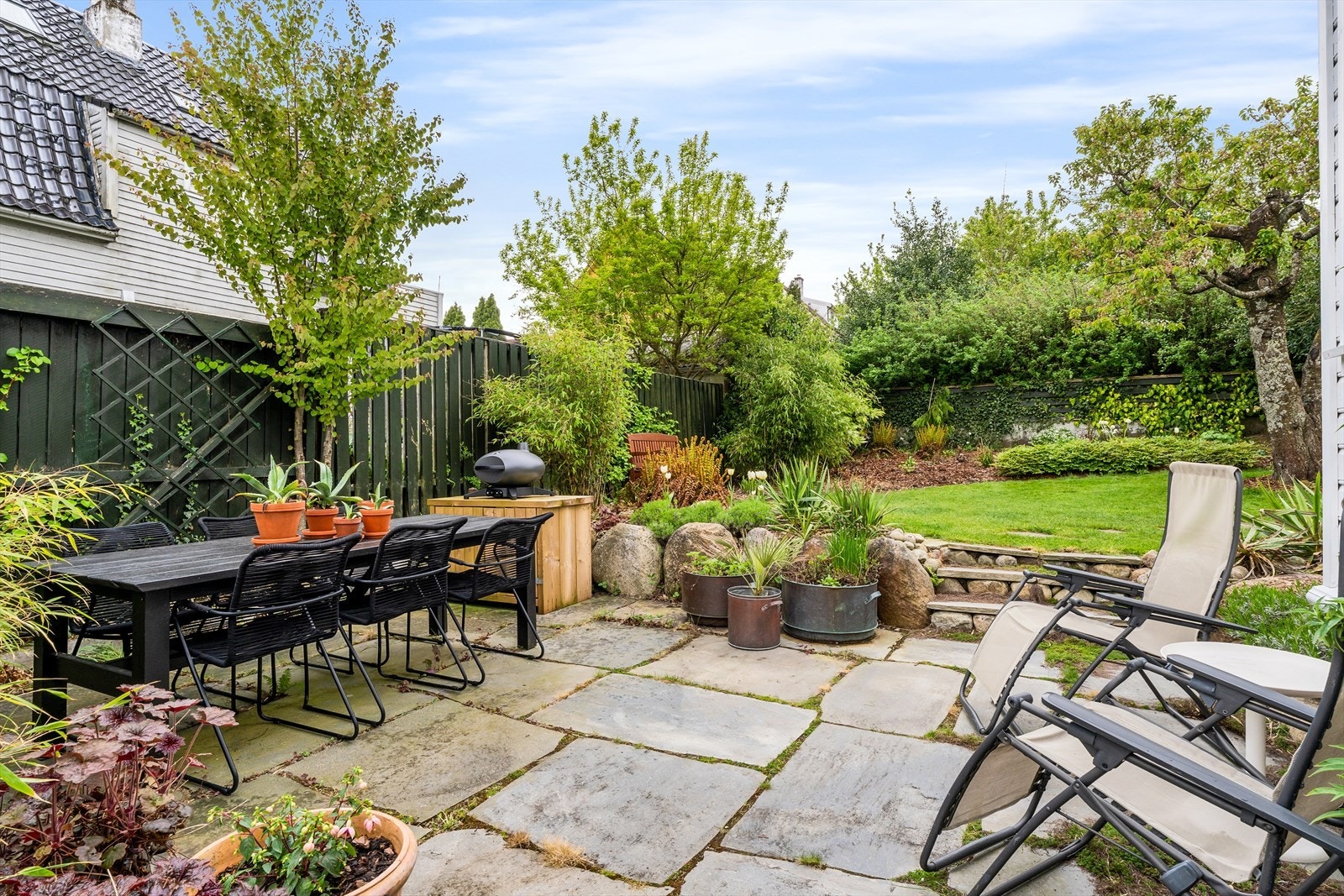 Skiferbelagt uteplass mot sør og terrasse ut fra kjøkkenet med tråkkheller i mellom. Galleribilde