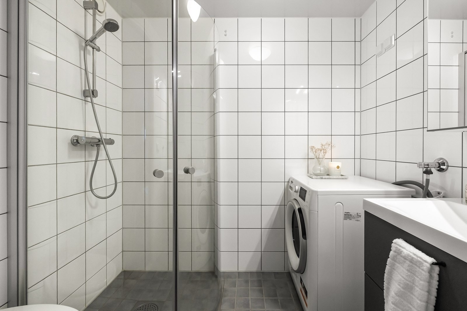 Pent helfliset bad innredet med wc, servant med møblement, speil, belysning og dusjnisje med foldedører. Galleribilde