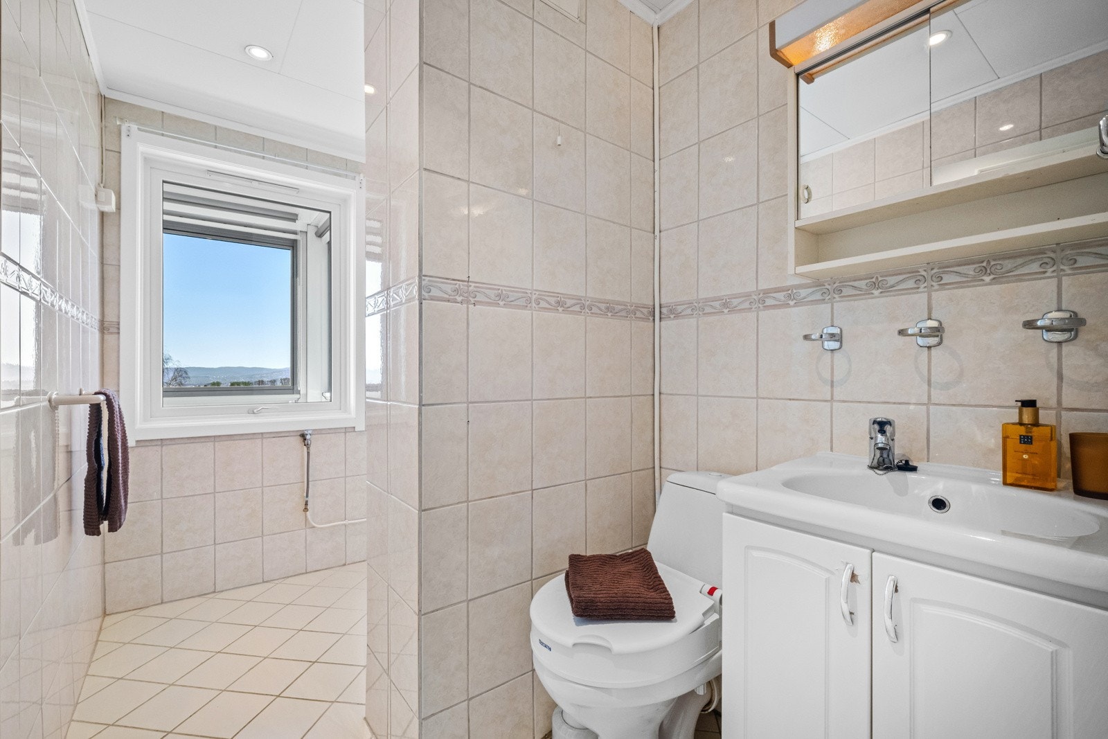 Badet er eldre med flislagte vegger og gulv, varmekabler, downlights og dagslys fra vindu mot balkongen. Galleribilde