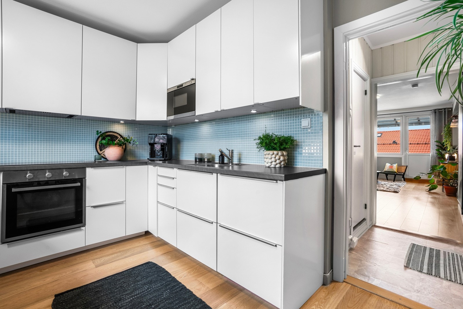 Kjøkkeninnredning har glatte, folierte fronter, laminat benkeplate med planlimt kum i rustfritt stål, downlights under overskap og fliser (mosaikk) over benkeplaten Galleribilde