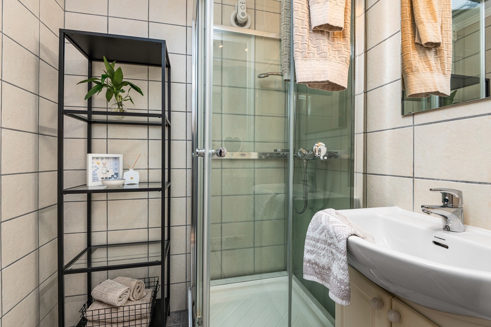 Badet er lyst og flislagt fra topp til tå med gulvvarme. Rommet er innredet med en praktisk hylle for oppbevaring av blant annet håndduker og baderomsartikler. Nåværende eier opplyser om nytt dusjkabinett som ble satt inn i 2018. Galleribilde