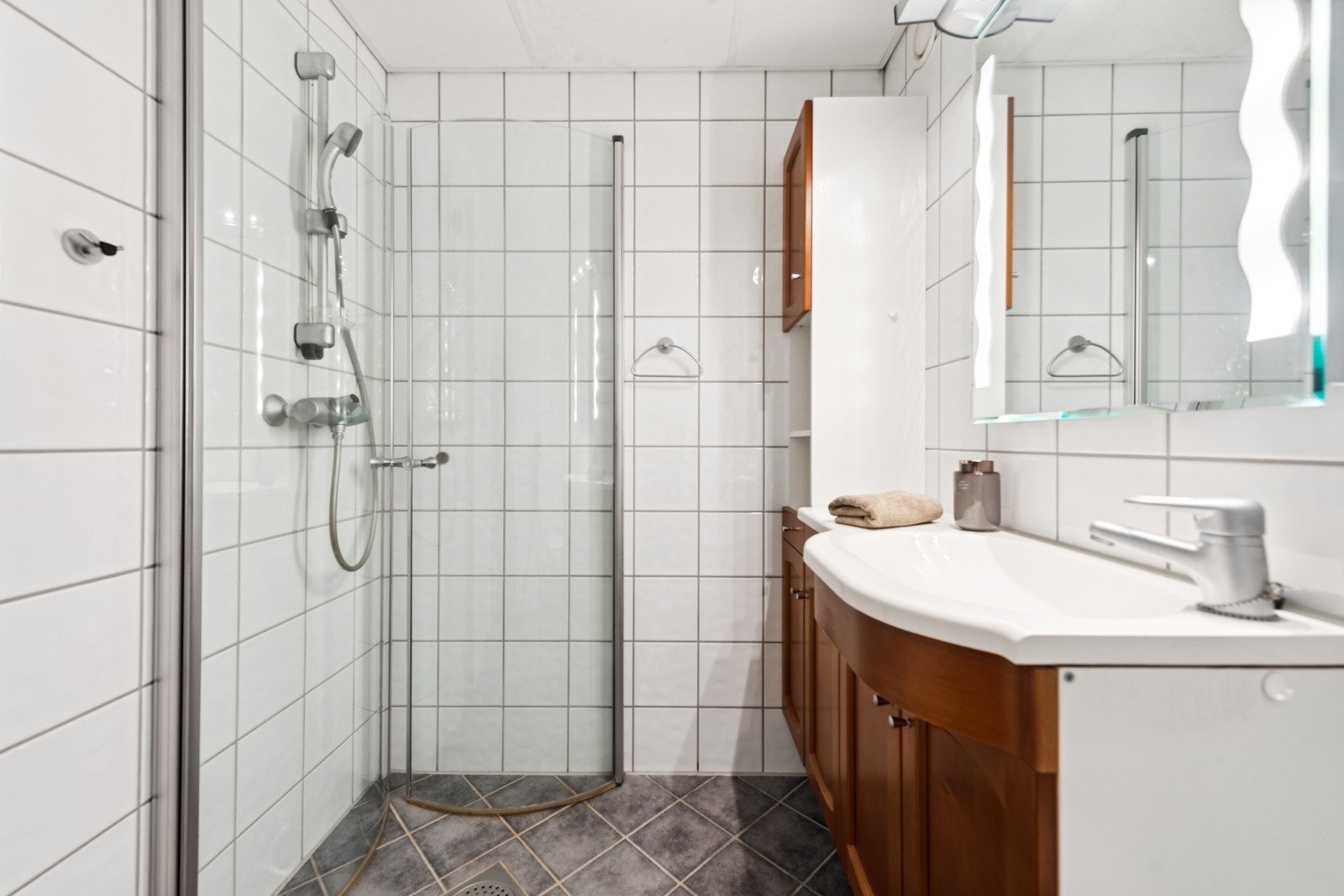 Pent flislagt bad og dusjhjørnet med inngsvingbare dører og vegghengt toalett. Galleribilde