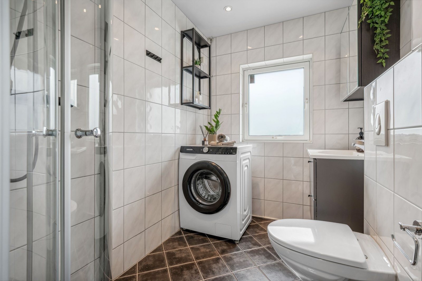 Badet er innredet med spotter i himling, dusjhjørne, veggehengt toalett, vask i seksjon og opplegg for vaskemaskin. Galleribilde