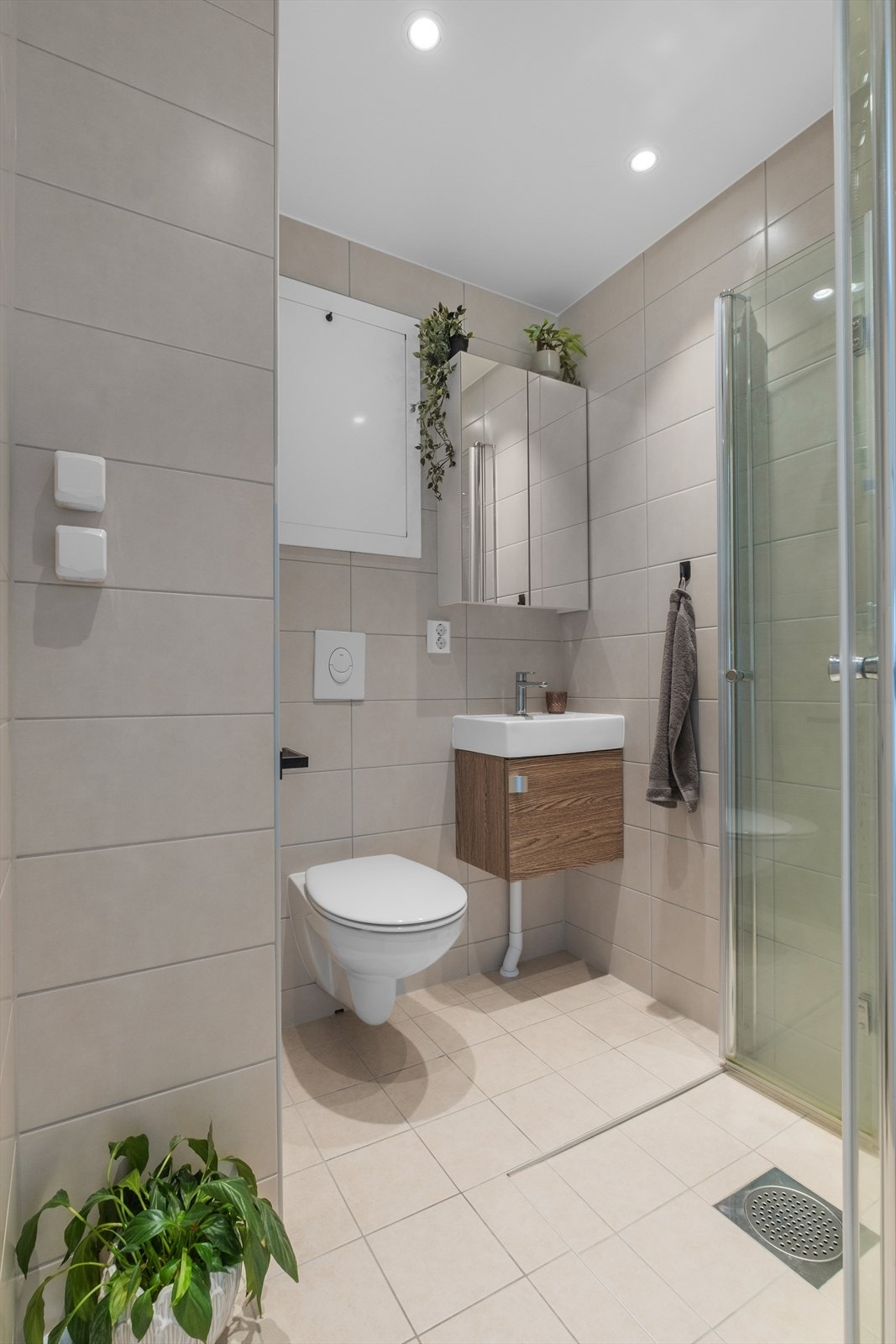 Moderne og stilrent bad fra 2022 med downlights i himling, fliselagte overflater og varmekabler i gulv. Badet er innredet med dusjhjørne med innfellbare dusjvegger, veggmontert wc og servant i innredning med speilskap. Galleribilde