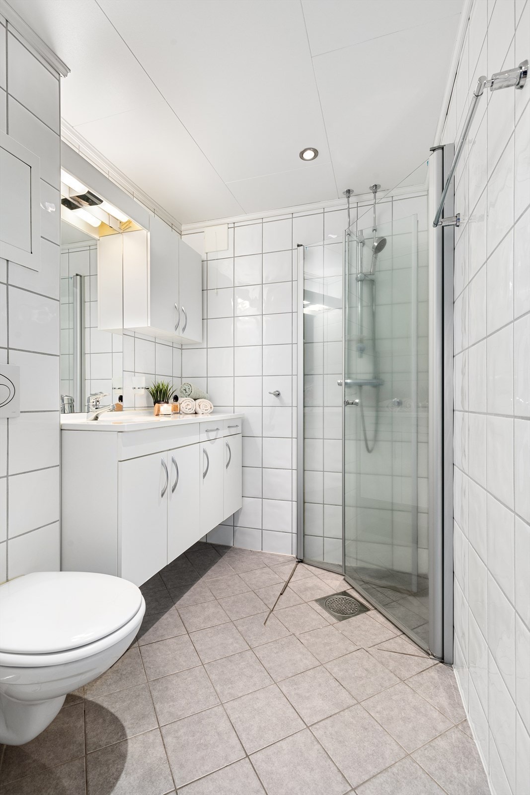 Badet er utstyrt med heldekkende servant med underskap, speil, veggskap, dusjnisje med innfellbare dører og toalett Galleribilde