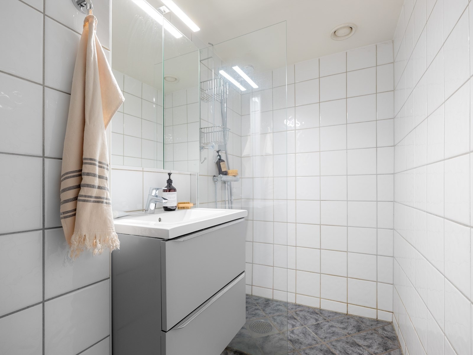 Det flislagte badet er lyst og pent ivaretatt med tidløse fliser og gulvvarme. Rommet ble pusset opp i regi av borettslaget i 2001. I ettertid er baderomsinnredningen skiftet i 2021. Galleribilde