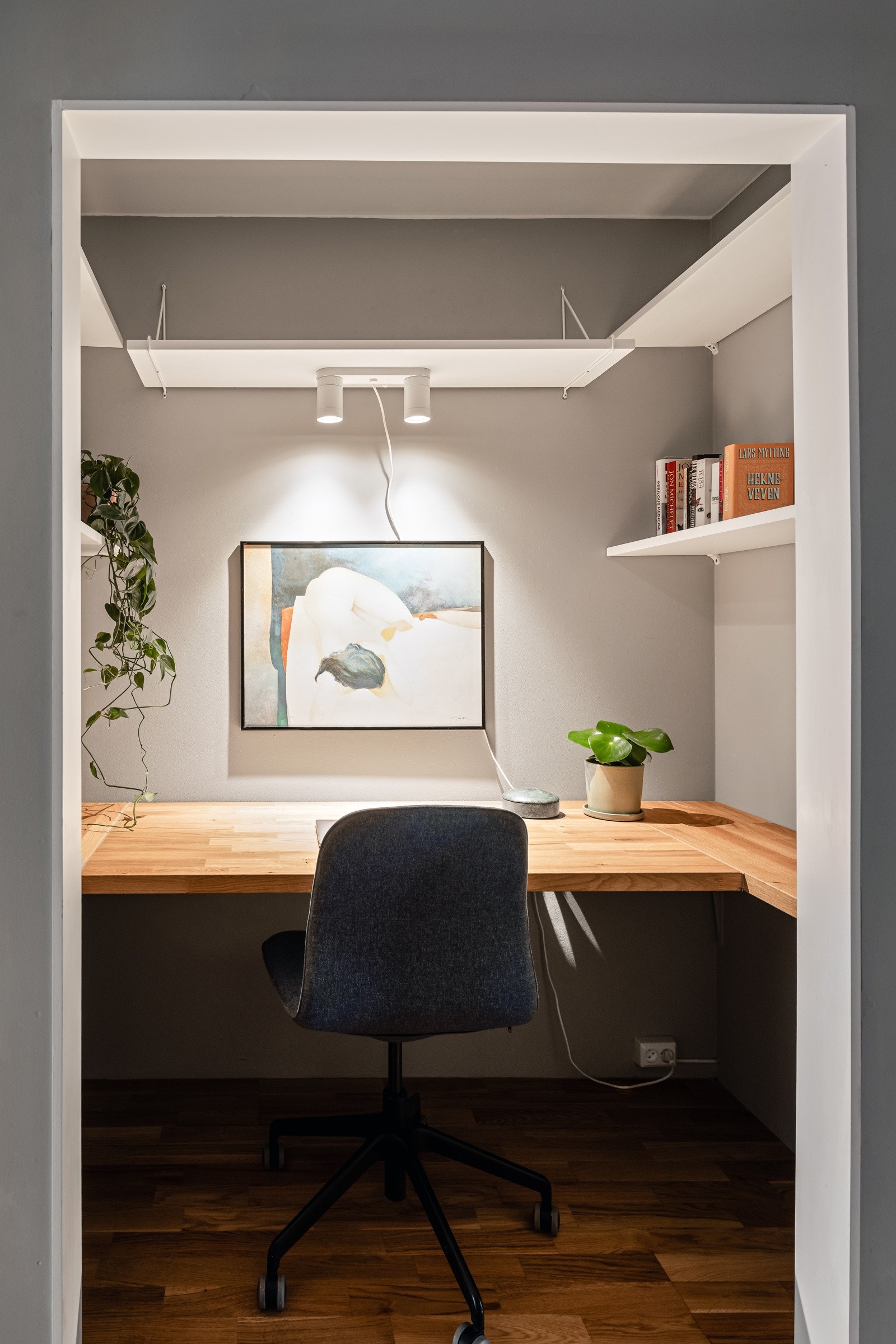 Dette er en praktisk arbeidsplass med plassbygget pult og vegghengte hyller for oppbevaring. Galleribilde